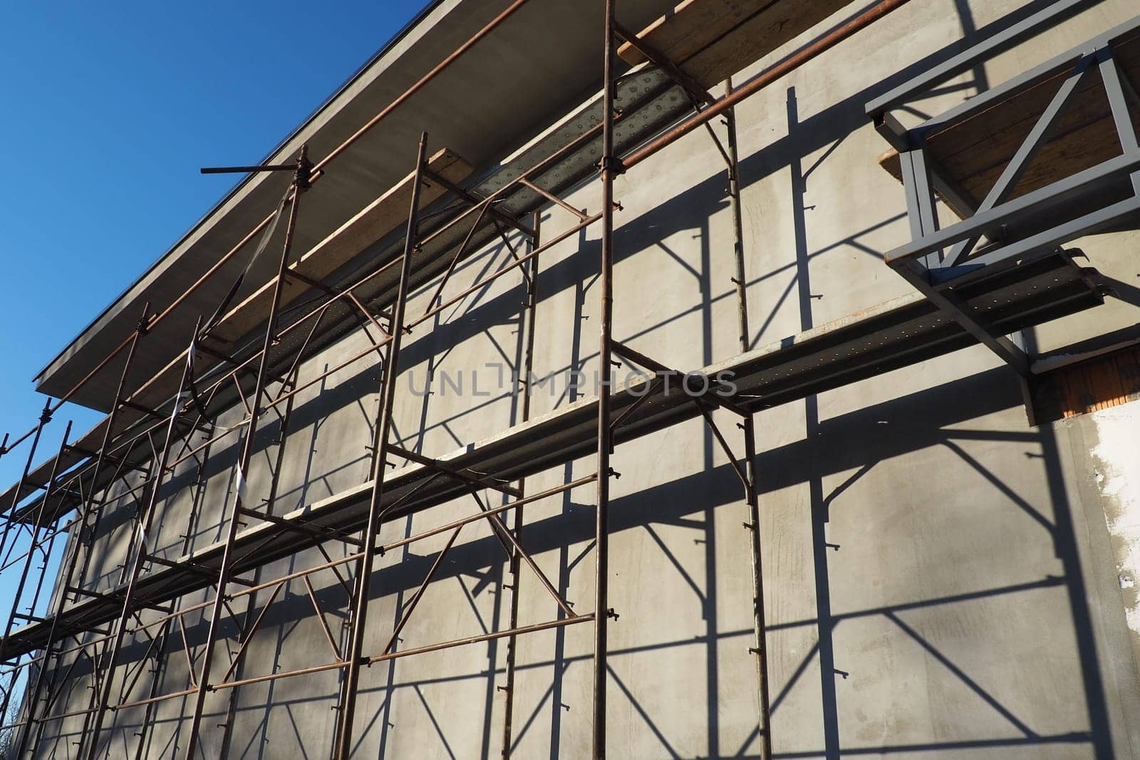 Scaffolding on a new one-story house. Facade works. Building bussiness. Low-rise private building. Plastering the wall of a building. Shop building. Metal production structures