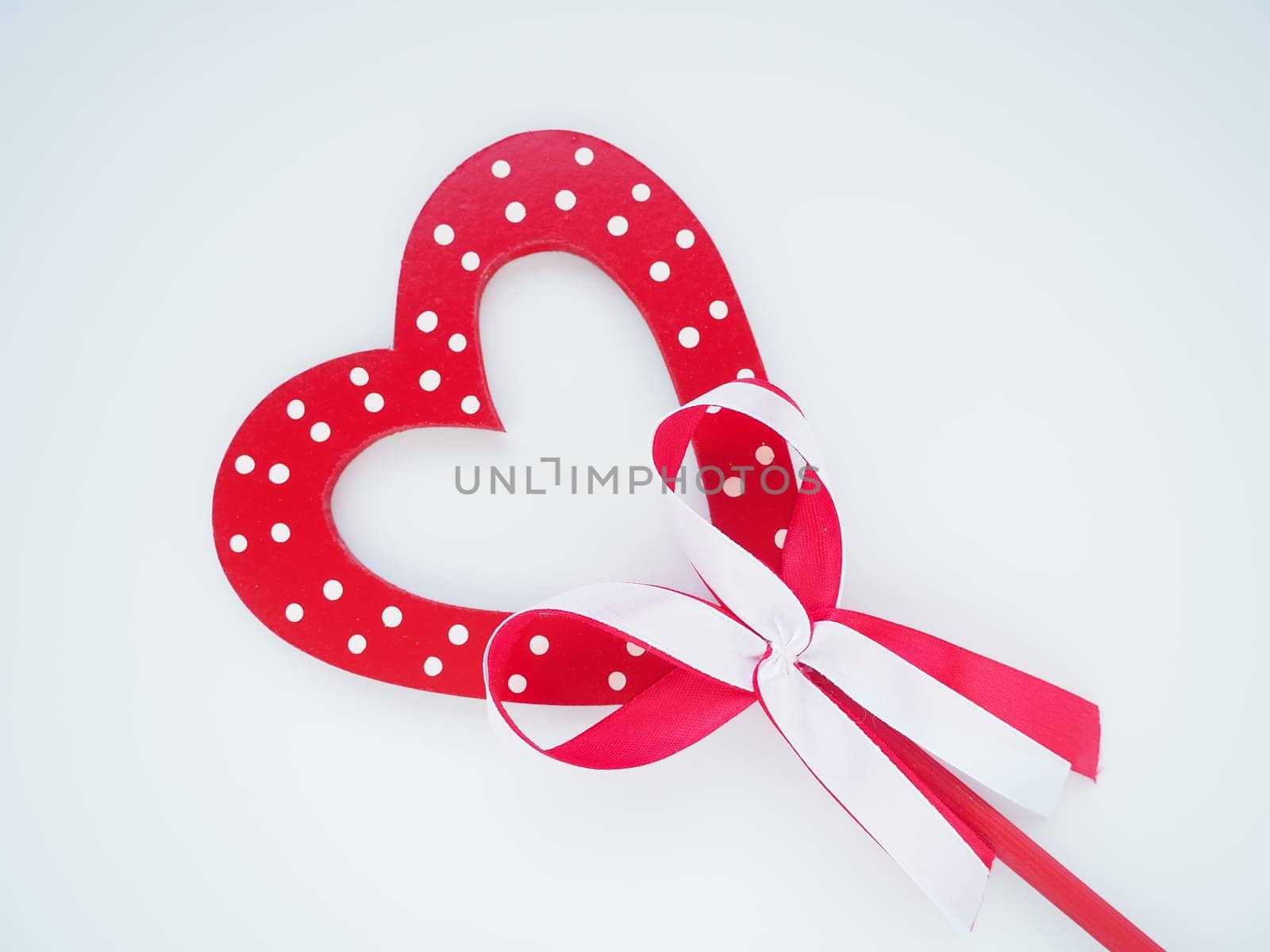 Valentine's day concept. Red wooden heart with white dots and ribbon bow on a stick. White background. A beautiful bow as a decoration. Love and relationships. Recognition or congratulations.