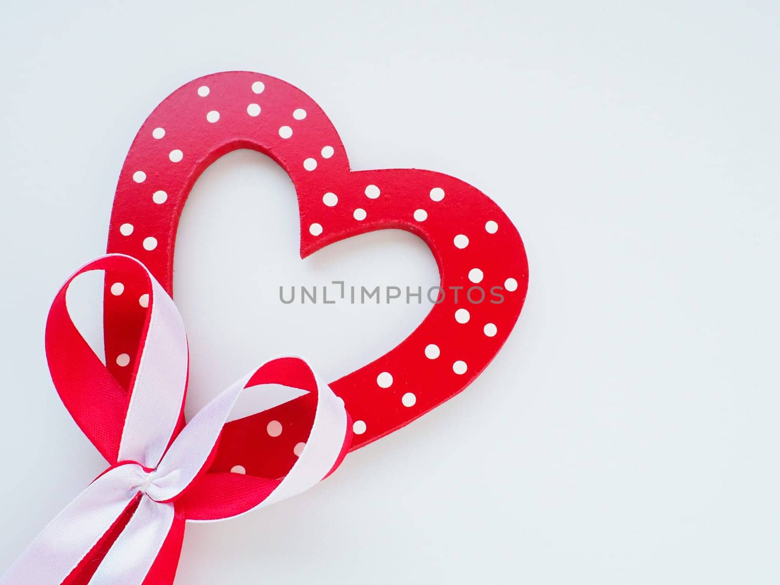 Valentine's day concept. Red wooden heart with white dots and ribbon bow on a stick. White background. A beautiful bow as a decoration. Love and relationships. Recognition or congratulations.