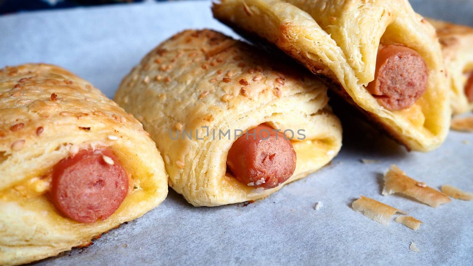 Sausages in the dough on a baking sheet with baking paper. Delicious fresh pies from the oven. Yeast dough culinary products with milk sausages. Sprinkling with sesame seeds