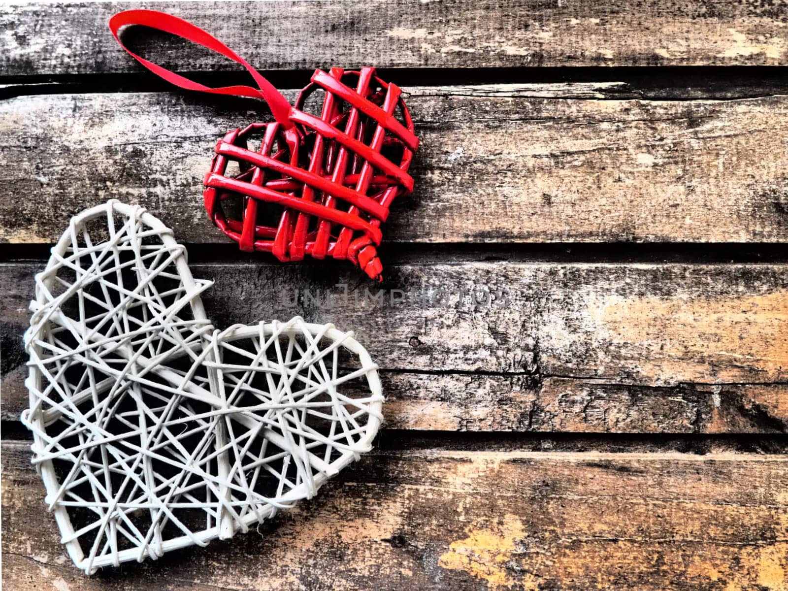 A wicker hearts a wooden background. Two red braided heart with hanging loop. White big heart. Two lovers. Valentine's Day Theme. Horizontal boards. copyspace. Flat lay.
