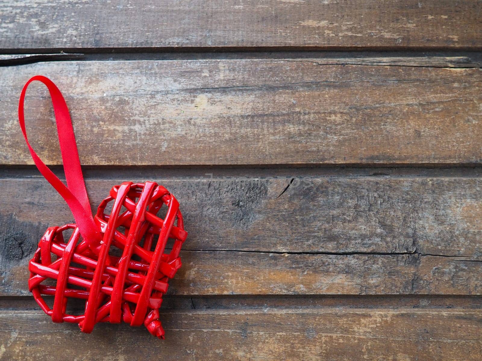 Love red wicker heart on wooden texture background. Valentines day greeting card. Top view with copy space. Red wicker heart made of twigs or straw. Flat lay. Declaration of love