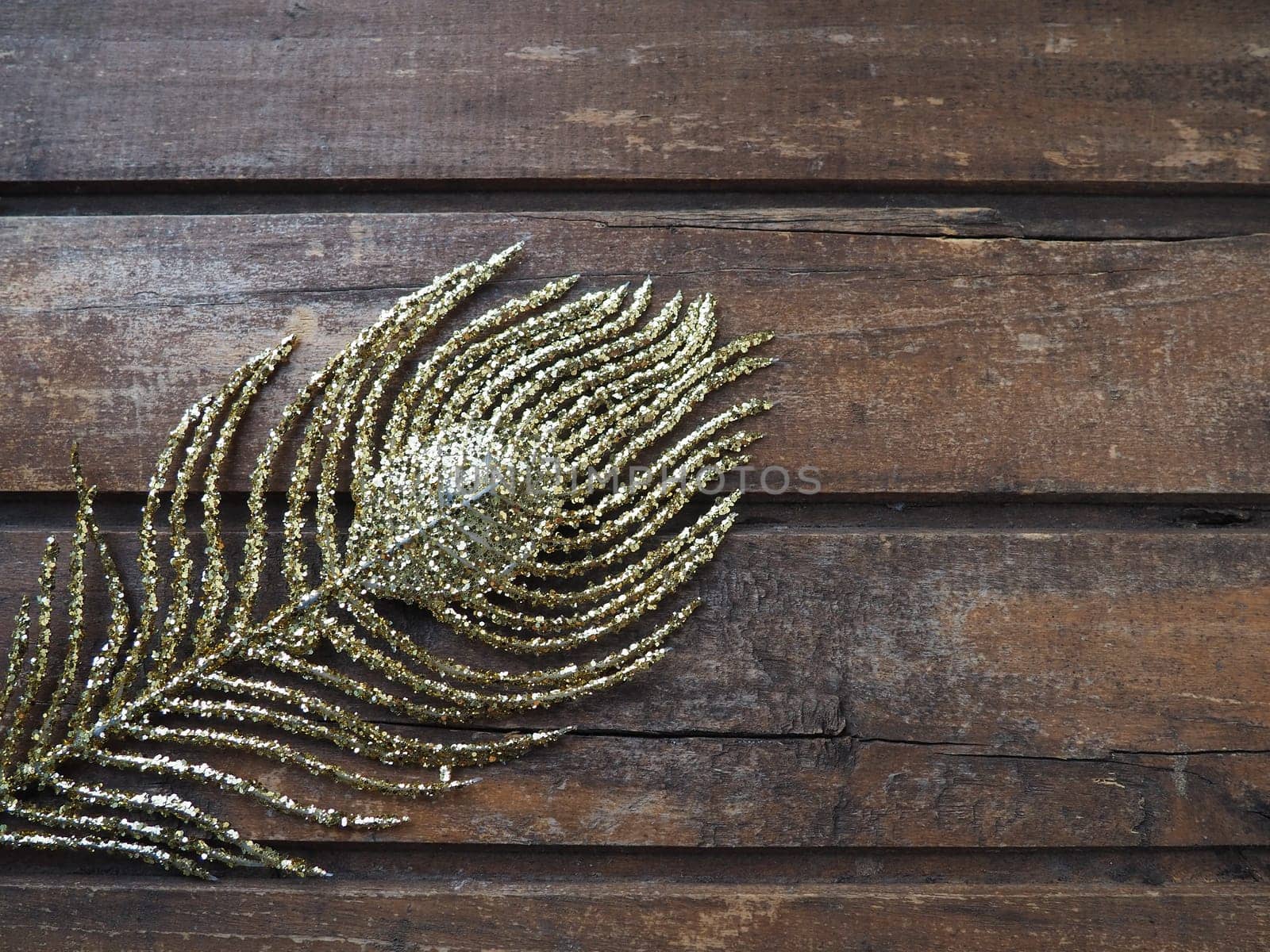 Golden peacock feather. Decorative gilded branch in the shape of a peacock's tail and eyelet. Wooden background. Festive decoration and beautiful carnival decor. Flat lay copy space.