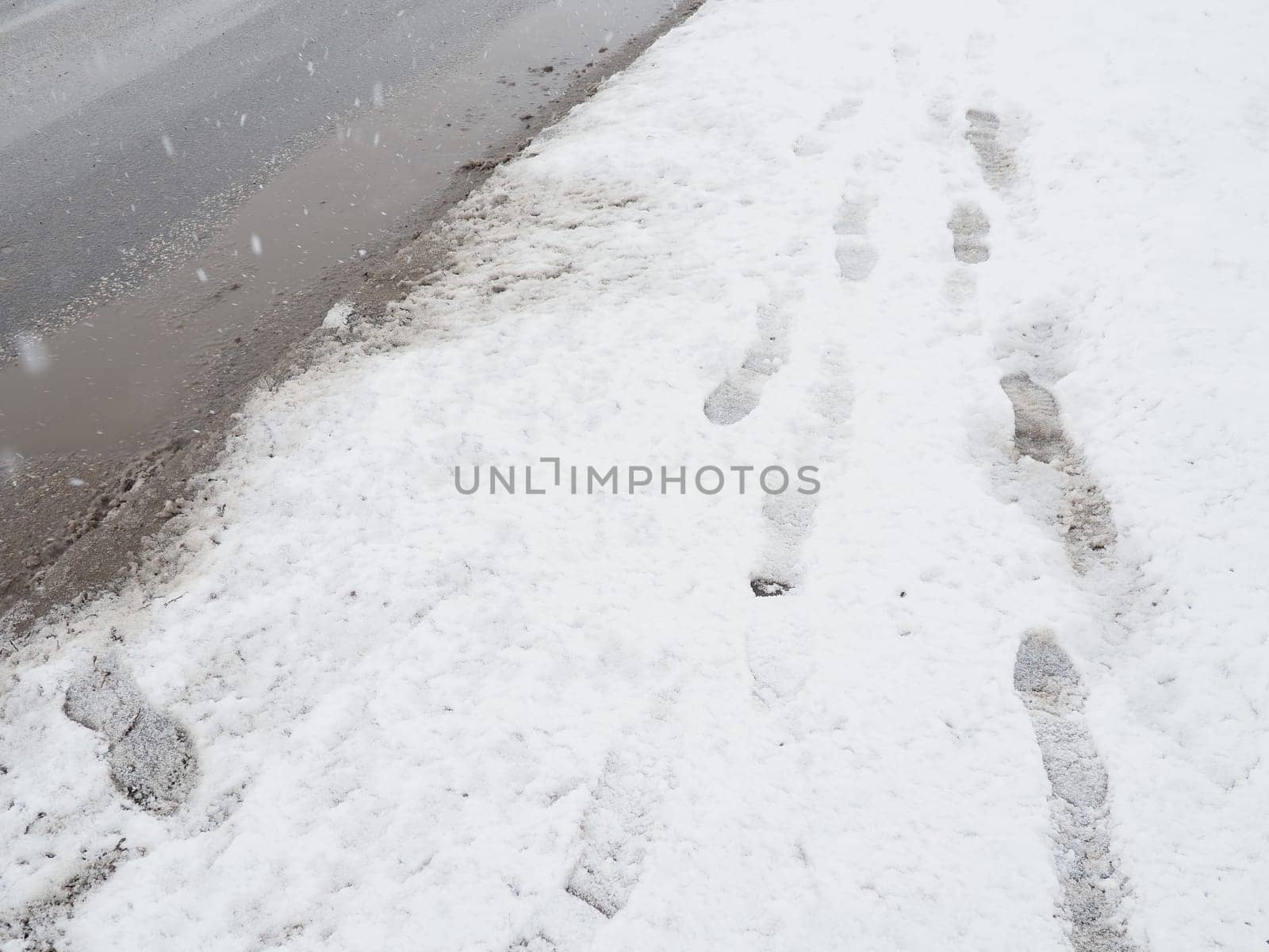 Roadside with a snowdrift. Difficult driving conditions. Wet slippery pavement with footprints. Dangerous ice. Muddy weather in winter. Car tire tracks. The work of municipal services for cleaning.
