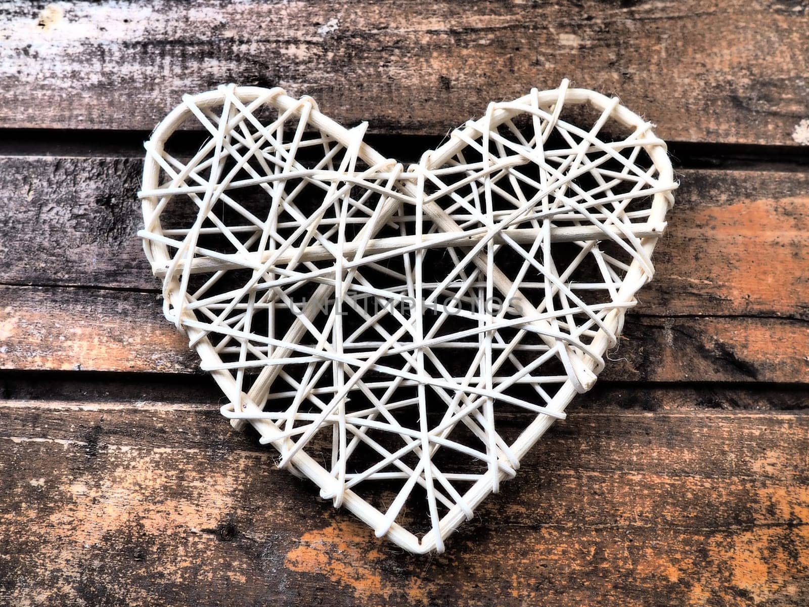 A heart woven from rustic light rods or threads. Wicker form handmade. Valentine's Day. Postcard. Wooden texture background. Love concept.