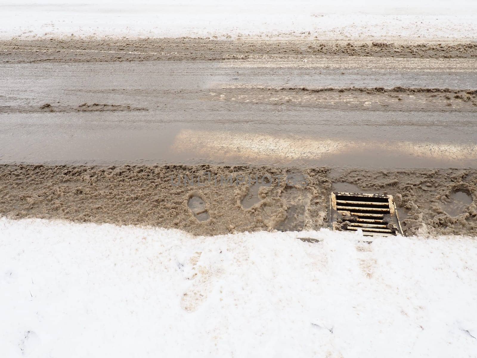 Snow, ice, slush and winter mud at a pedestrian crossing. The air temperature is about 0. Difficult driving conditions. Braking distance of the car. Underground drain with metal grate. Snow melting.