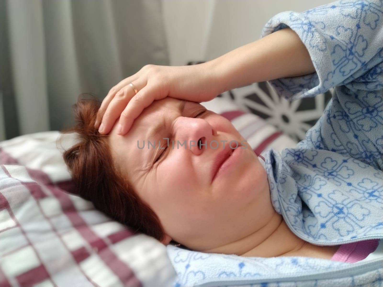 Sick woman in bed. Headache, runny nose and cold. Paleness of the face and faintness of the body. Feeling unwell. The patient lies on a pillow, holding forehead with his hand. Sharp pain and grimace.