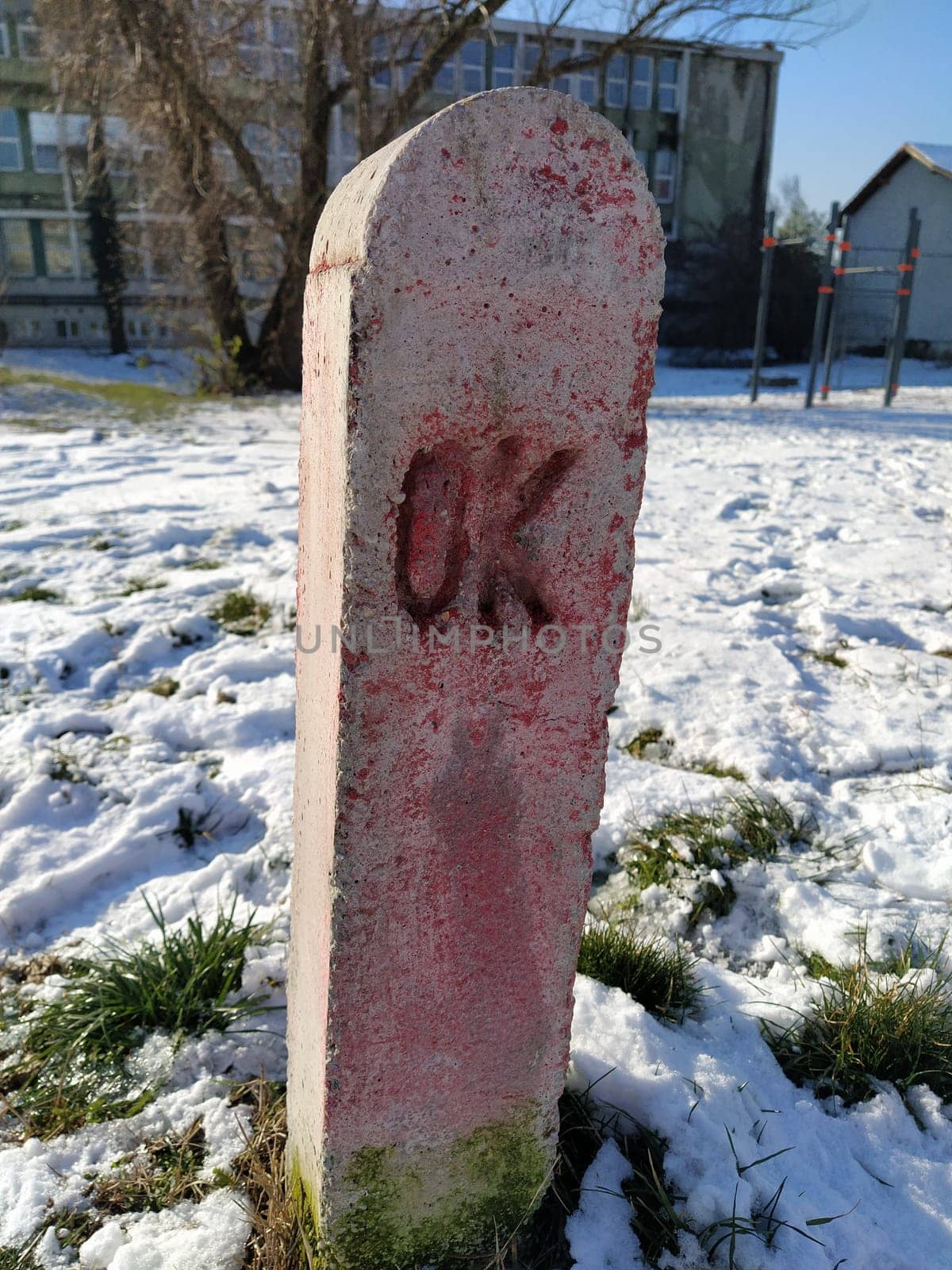 Strange concrete pillar in the city. Pink monument on the grave with the inscription OK. City engineering communications and designations. Snow with footprints