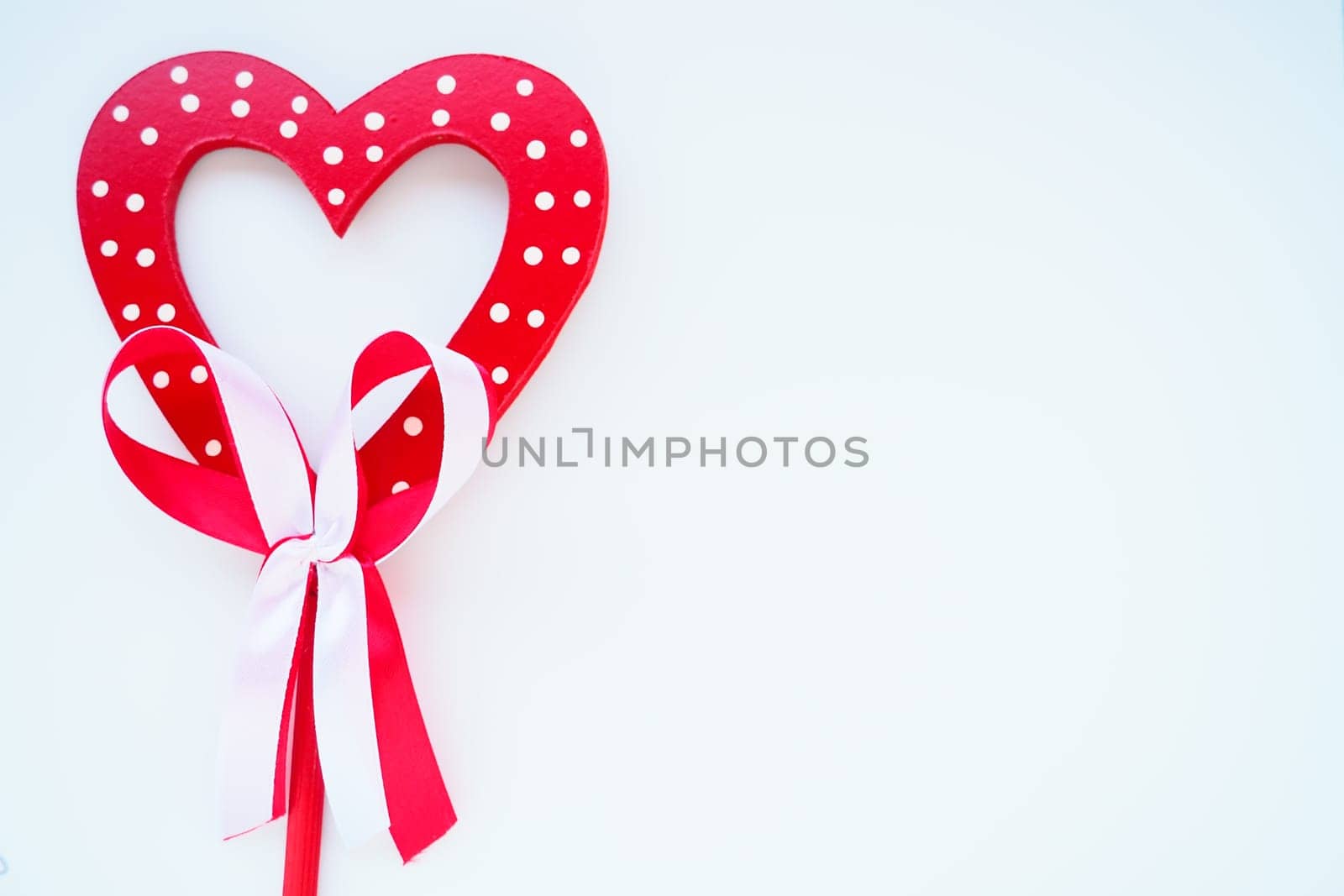Valentine's day concept. Red wooden heart with white dots and ribbon bow on a stick. White background. A beautiful bow as a decoration. Love and relationships. Recognition or congratulations.