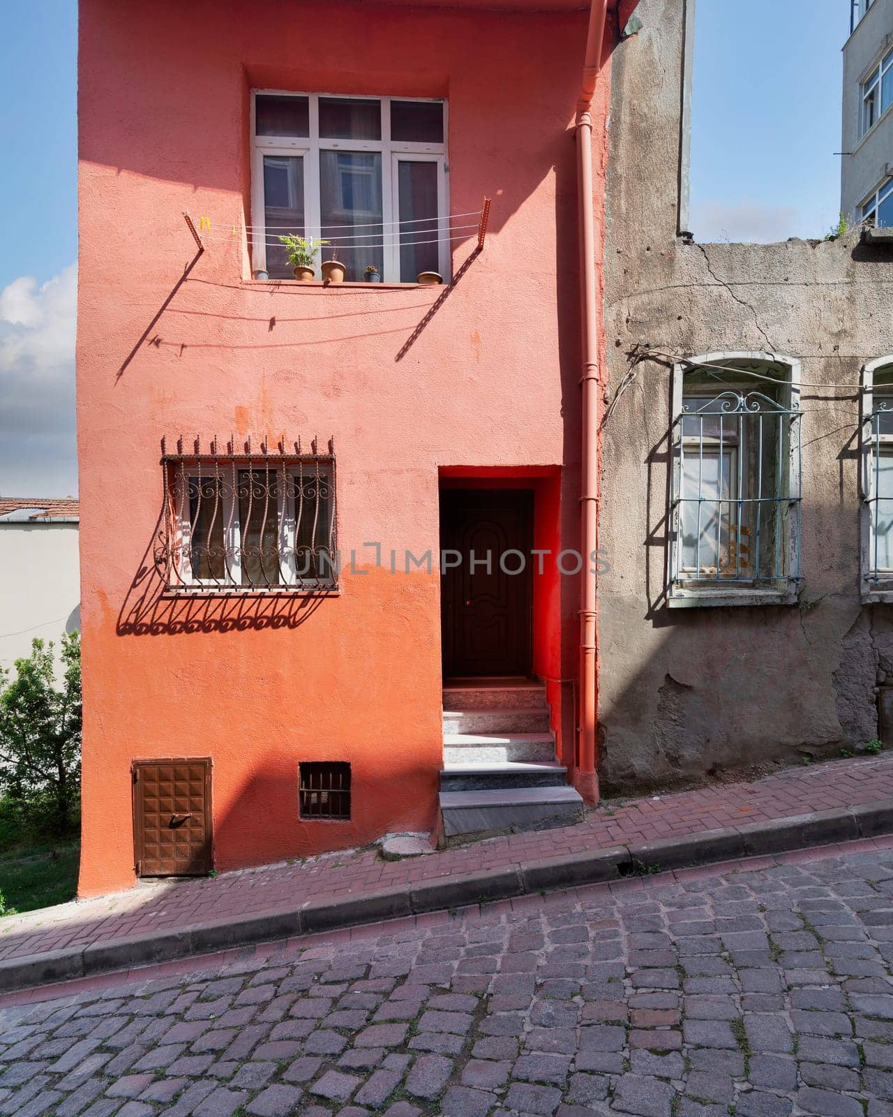 Exterior facade of old residential building with walls painted in orange, and wrought iron windows, at a narrow cobblestone street, Balat district, Istanbul, Turkey