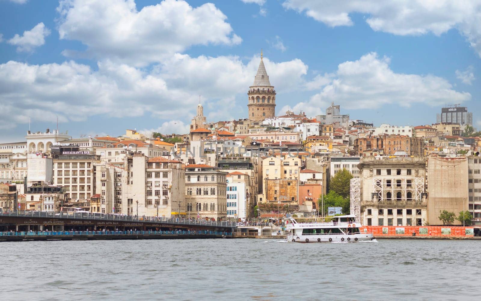 Istanbul, Turkey - August 25, 2022: City skyline including Galata Bridge with traditional fish restaurants in the passage under the bridge, and Galata Tower in the far end