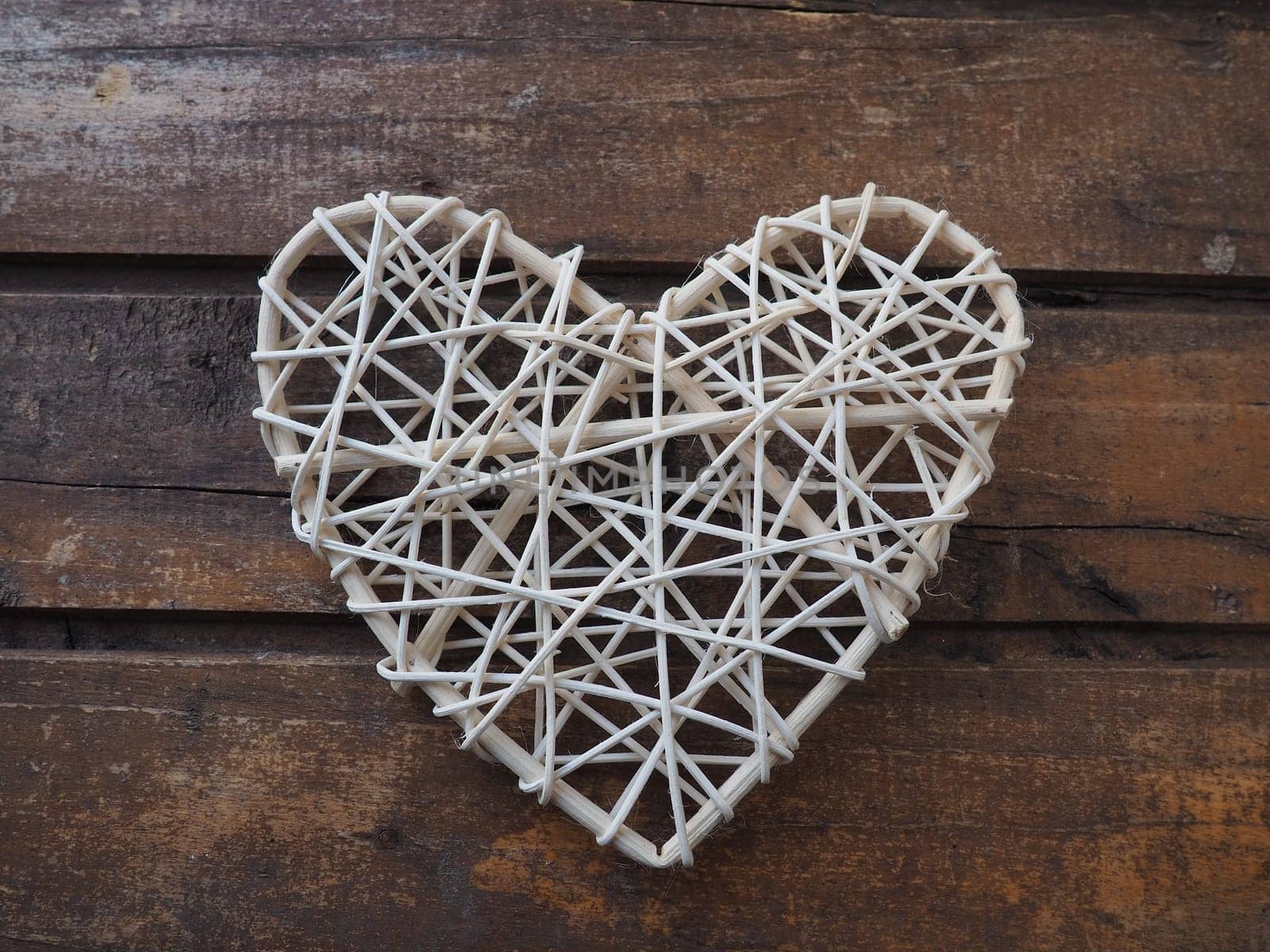 A heart woven from rustic light rods or threads. Wicker form handmade. Valentine's Day. Postcard. Wooden texture background. Love concept.