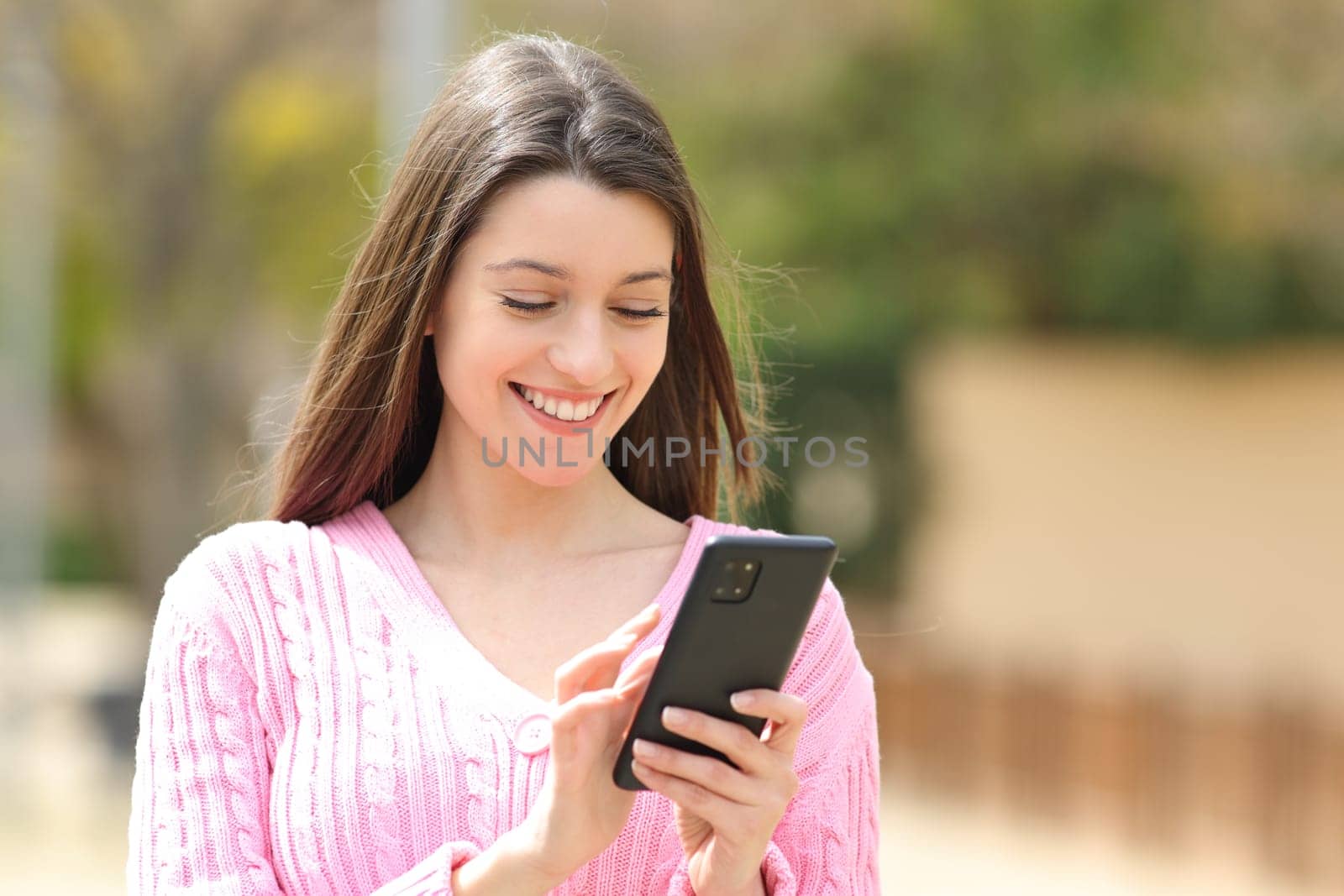 Happy teen in pink using phone walking in the street