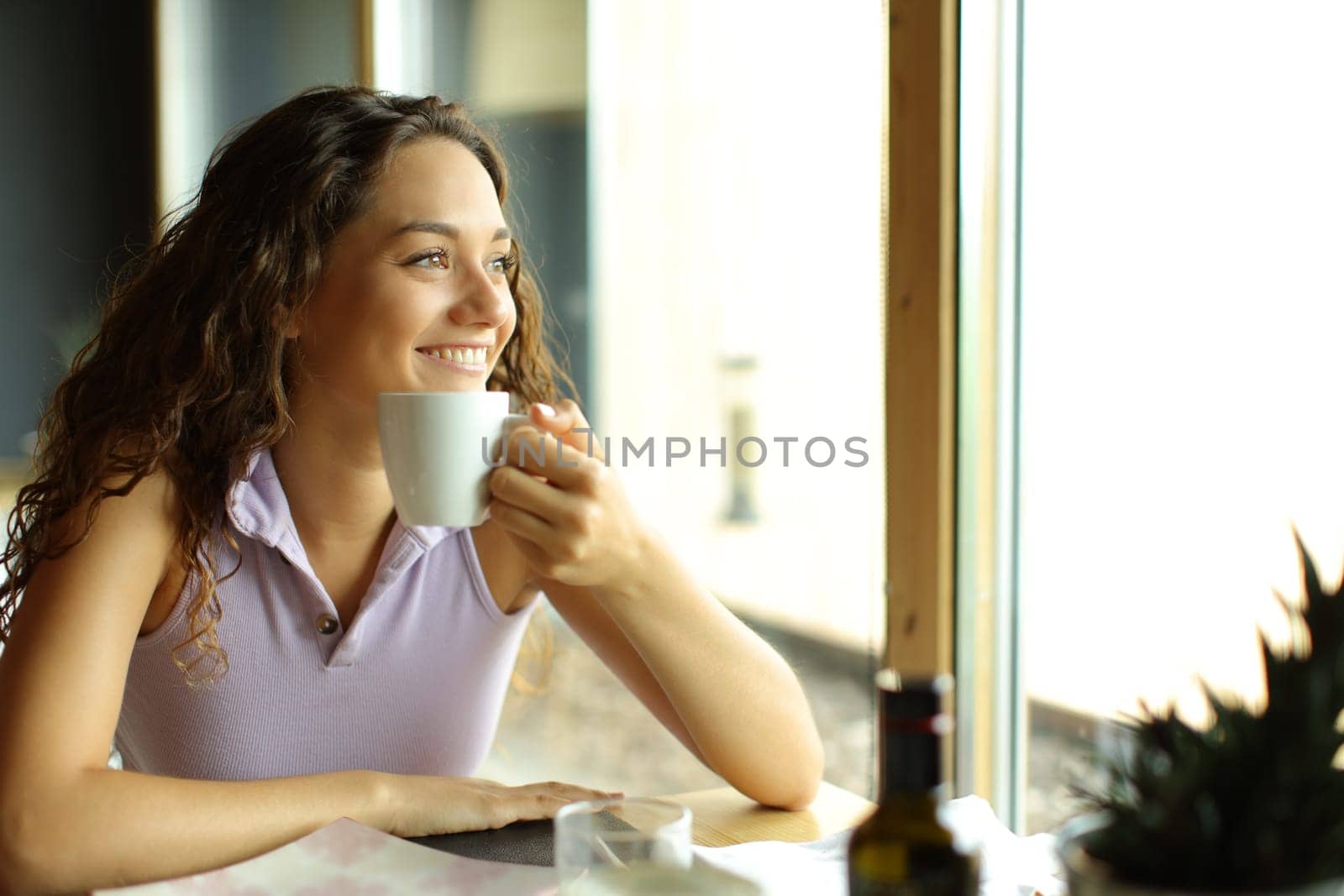 Happy woman holding coffee cup in a restaurant looks away through a window