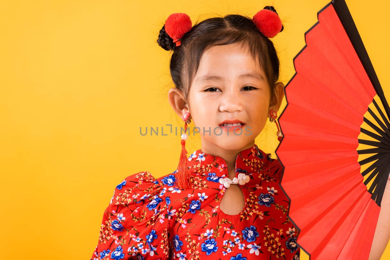 Chinese New Year. Happy Asian Chinese little girl smile wearing red cheongsam holding fan, Portrait children in traditional dress, studio short isolated on yellow background