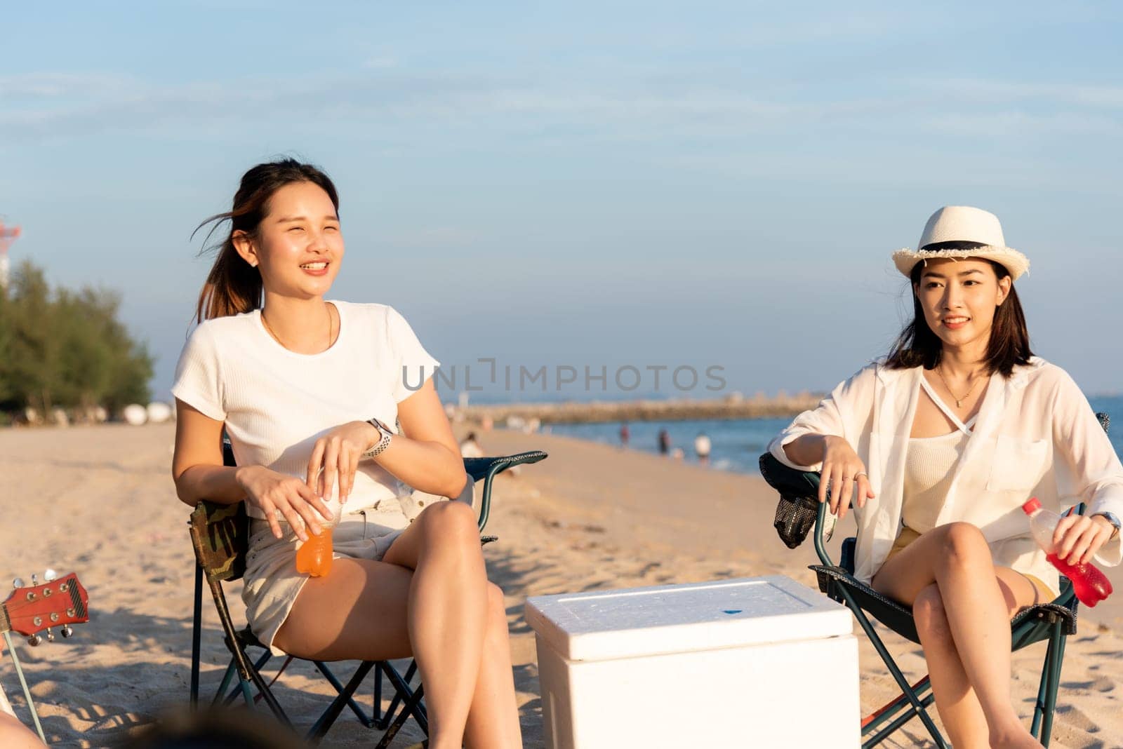 Happy friends with drinks in camp and laughing together in holidays on sand beach near camping tent vacation time at sunset, Young Asian group woman and man in summer travel outdoor