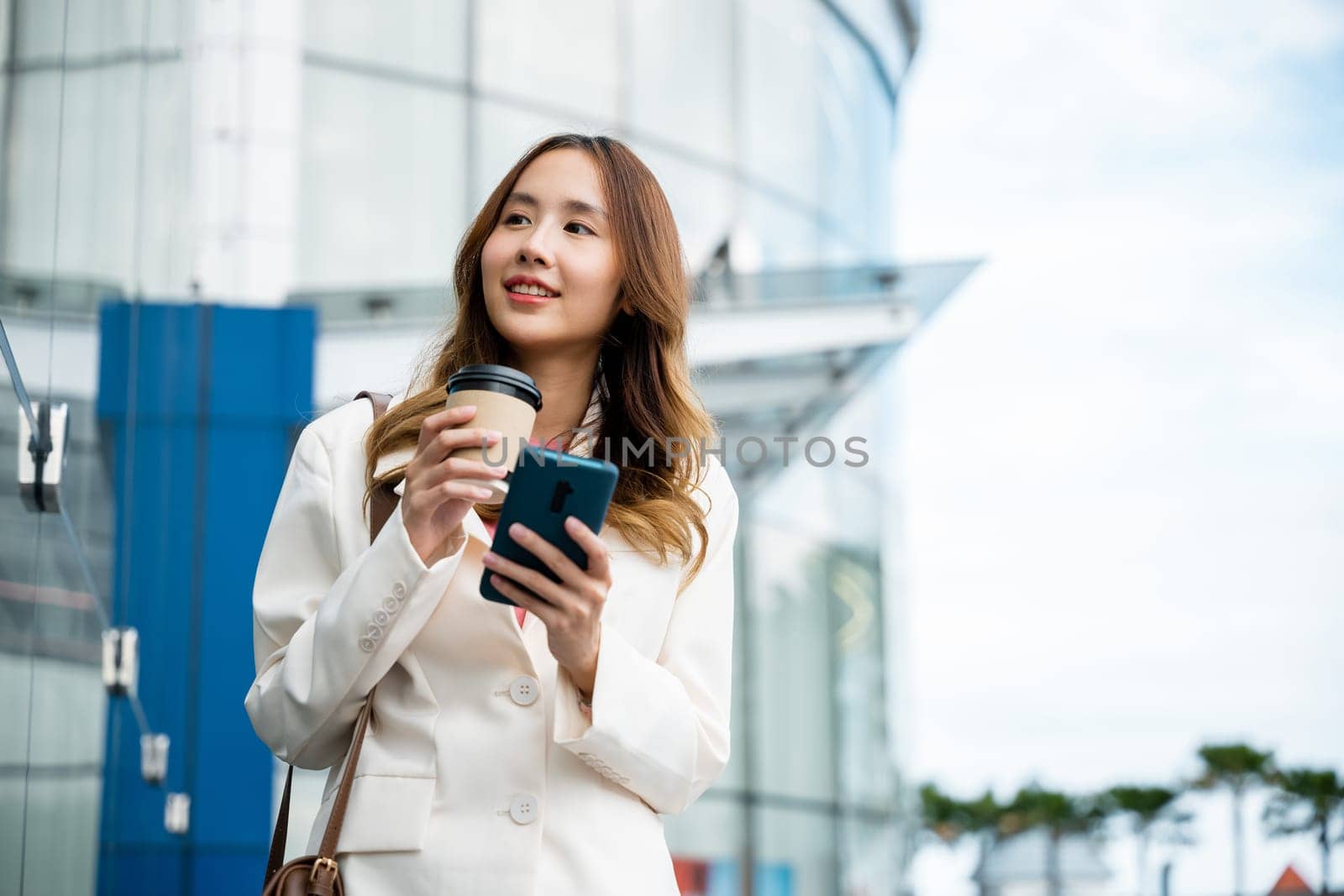 Asian businesswoman with smartphone and cup coffee standing street front building near office, Portrait woman smiling holding smart mobile phone with coffee take away going to work early in morning