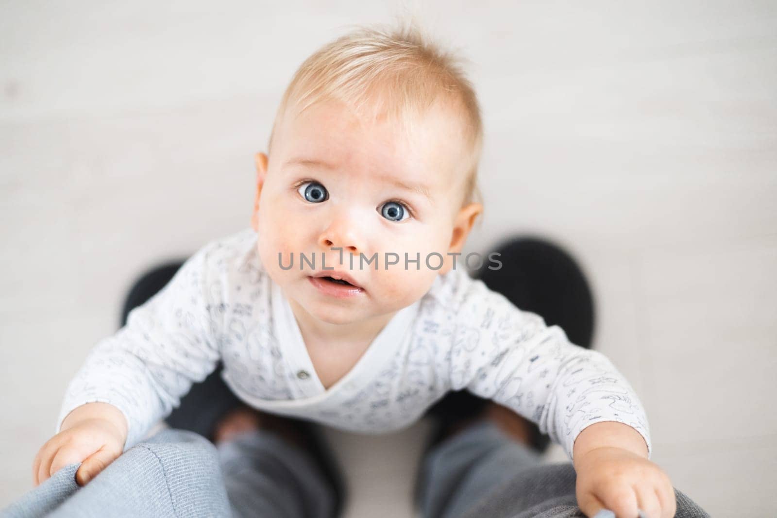 Top down view of cheerful baby boy infant taking first steps holding to father's sweatpants at home. Cute baby boy learning to walk.
