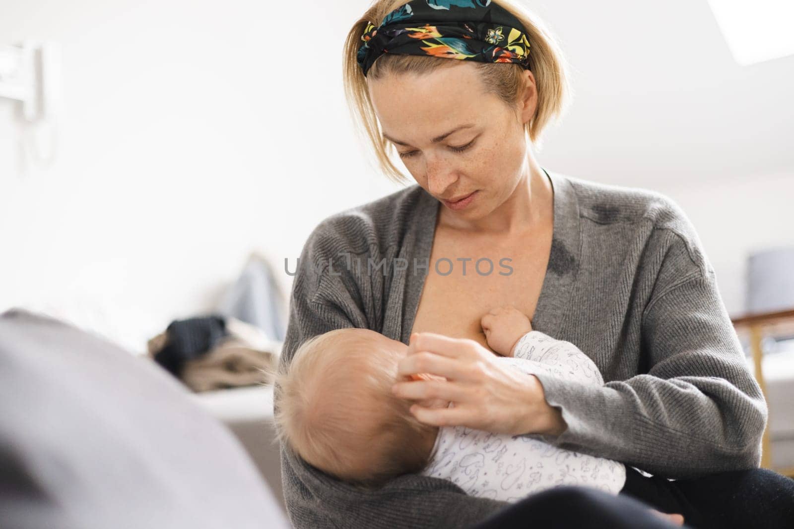 Young woman breastfeeding her infant baby boy casualy sitting on child's playing mat on living room floor at home