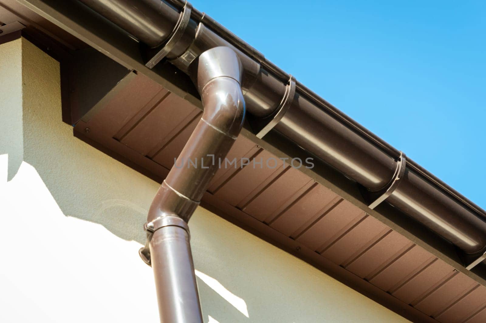 Brown pvc gutter connected to downpipe on roof edge and sky.