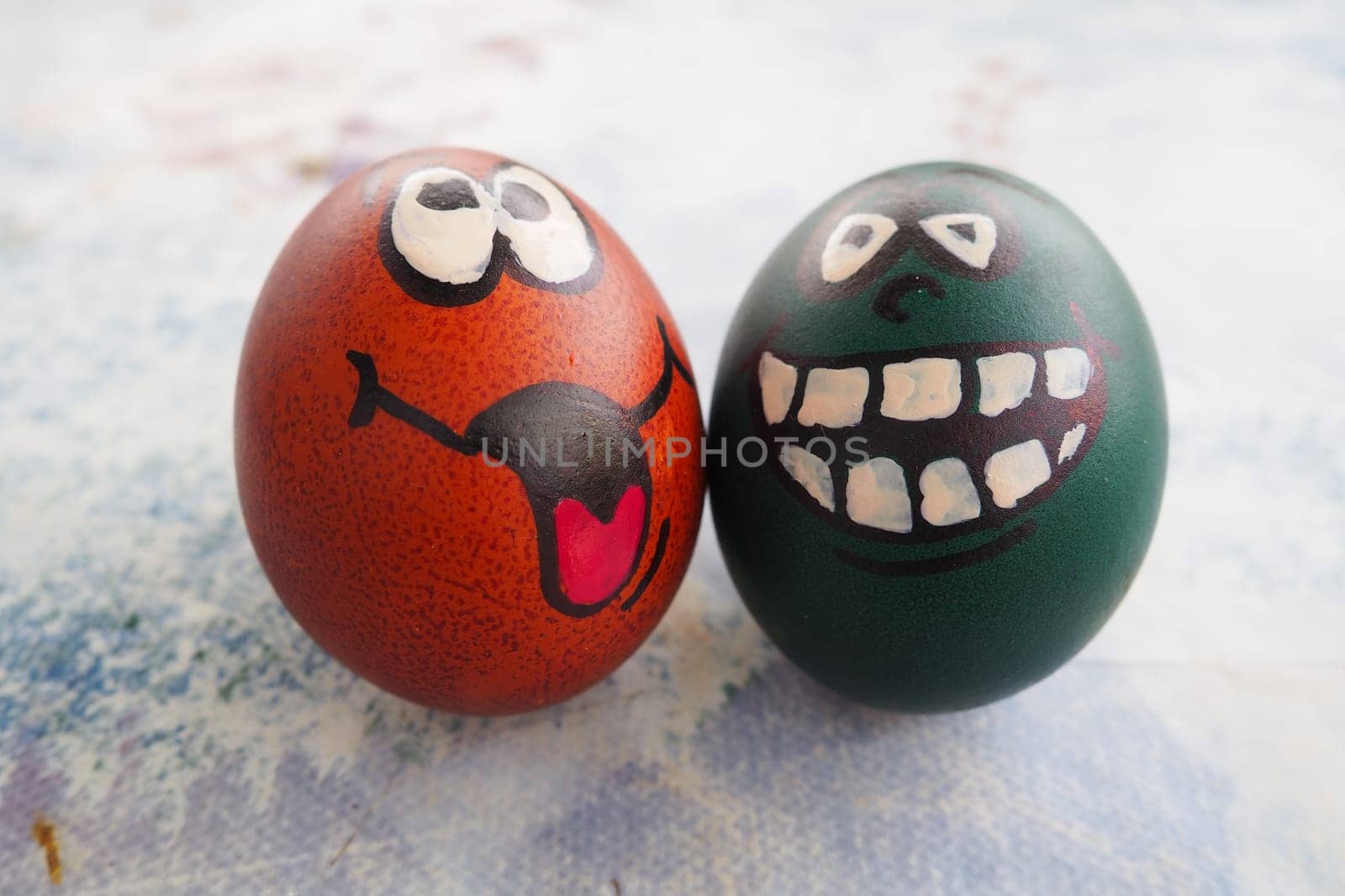 Easter eggs dyed green and brown with painted laughing faces. Funny grimaces with eyes, tongue and big white teeth. Scary face for Halloween. Emoticon for Easter. Light abstract background