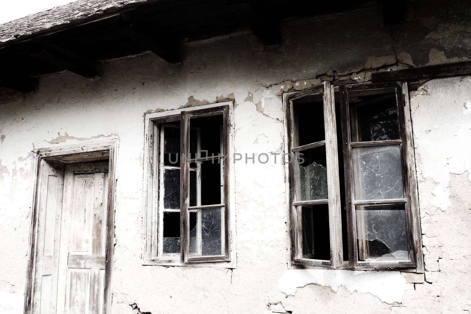 Abandoned spooky old house. Wooden windows and doors. The hut is a mud hut. Samani house. White stucco plaster. Halloween theme. Aging, loneliness, departure, war and devastation. Ukraine, Donbass.