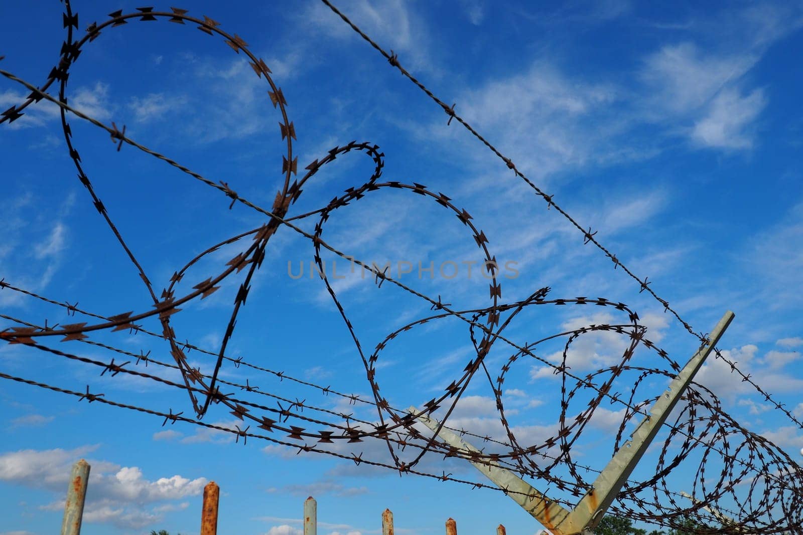 Barbed wire against the blue sky. Barbed wire is a wire or a narrow strip of metal with sharp spikes. Device of barriers. The concept of freedom, protection of property, violence, imprisonment.