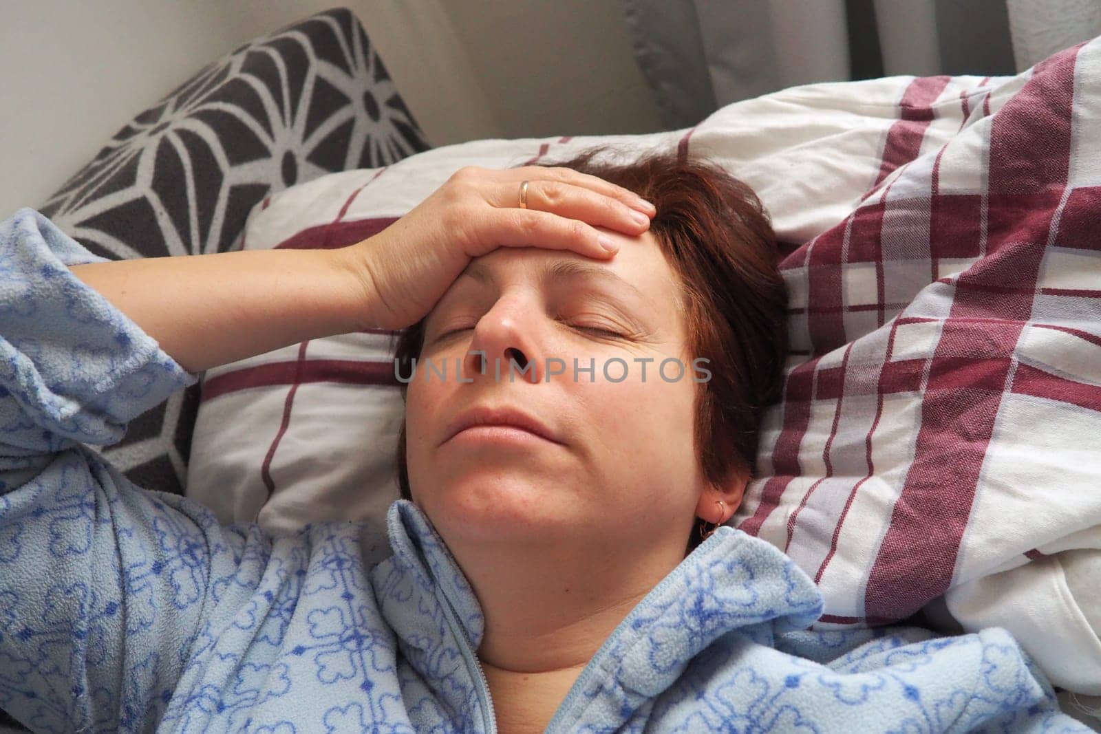 Sick woman in bed. Headache, runny nose and cold. Paleness of the face and faintness of the body. Feeling unwell. The patient holds his forehead with his hand and covers his eyes.