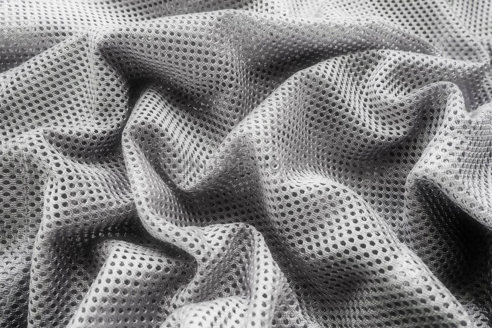 Synthetic fabric with holes laid in waves. Beautiful drape. Fabric for curtains, interior design, and decor. Wrinkled gray fabric