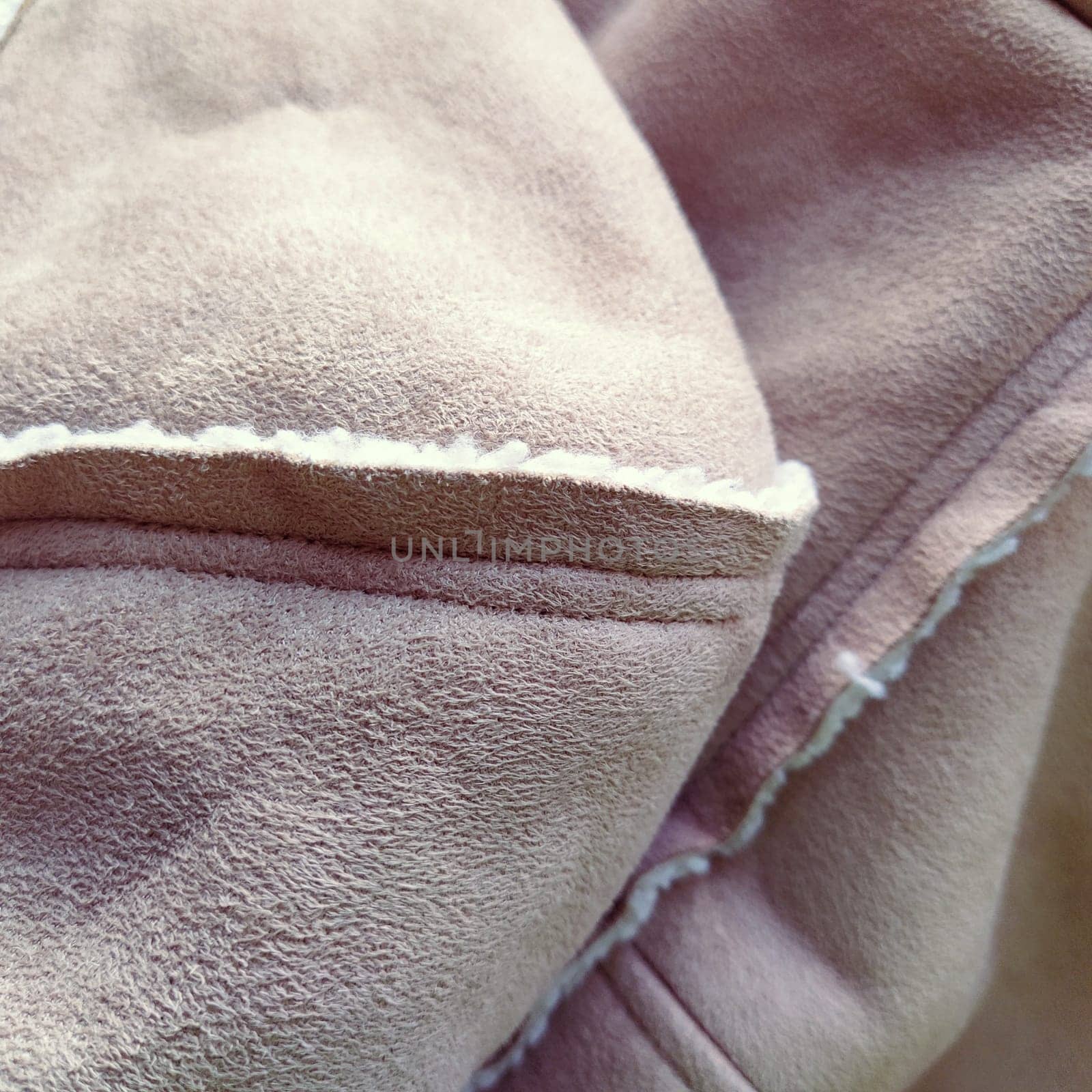 Suede outerwear with a hood. Beige faux suede with sheepskin on the fold of a demi-season garment. seams in the material. Clothing industry and fashion