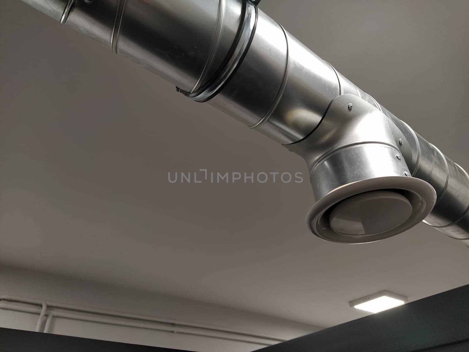 Extractor hood in a public toilet. Round metal pipe with gray air extractor. Engineering ventilation systems. Galvanized pipes under the ceiling of the room. Plastic round tip.