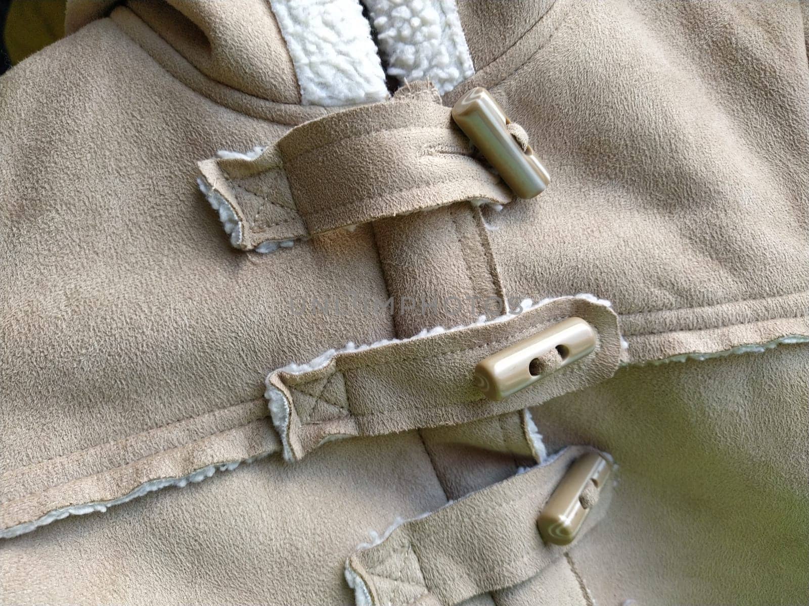 Suede outerwear. Overhead loops for buttons. Hidden zipper. Beige faux suede with sheepskin on the fold of a demi-season garment. seams in the material. Clothing industry and fashion