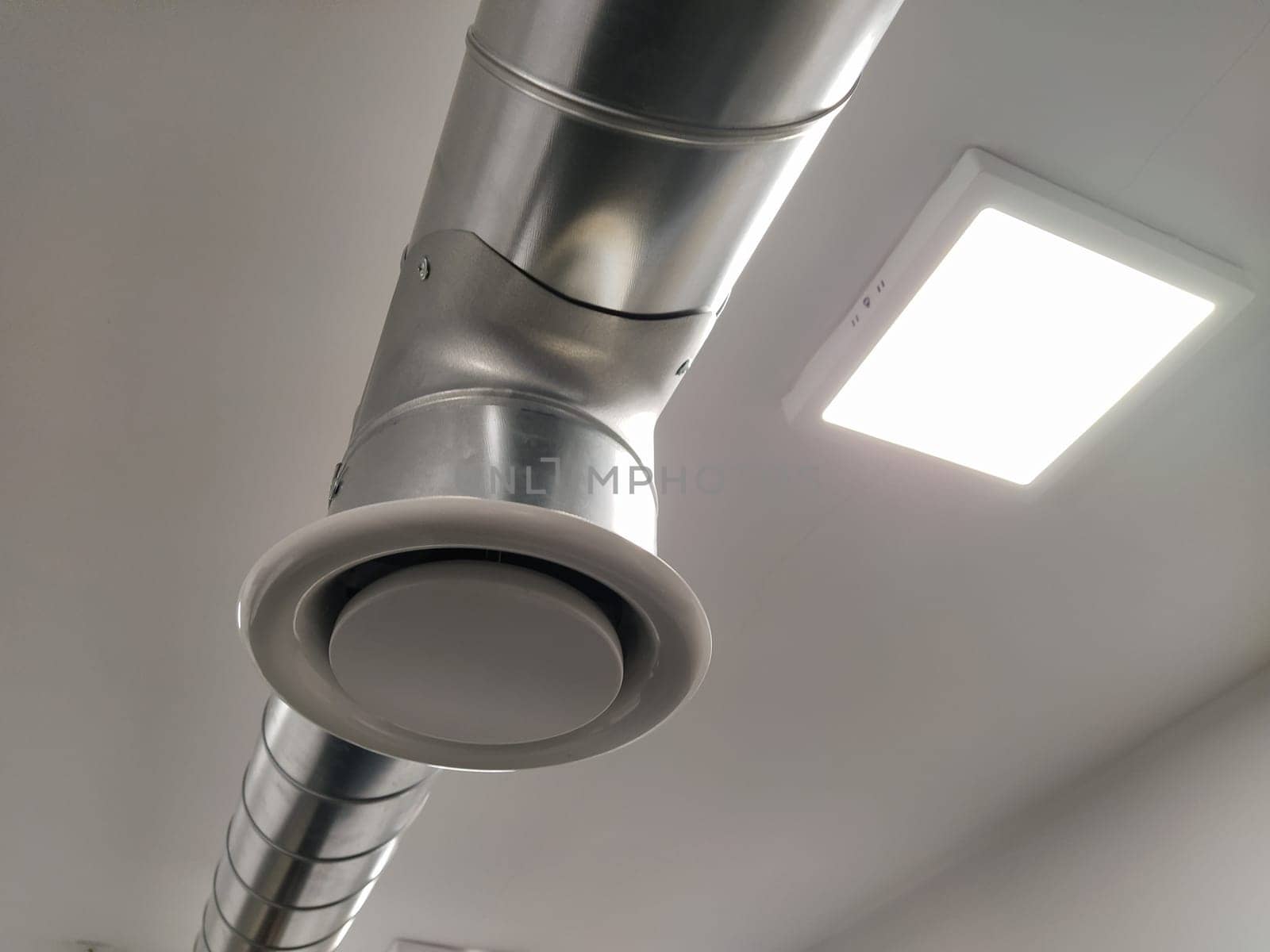 Extractor hood in a public toilet. Round metal pipe with gray air extractor. Engineering ventilation systems. Galvanized pipes under the ceiling of the room. Plastic round tip.