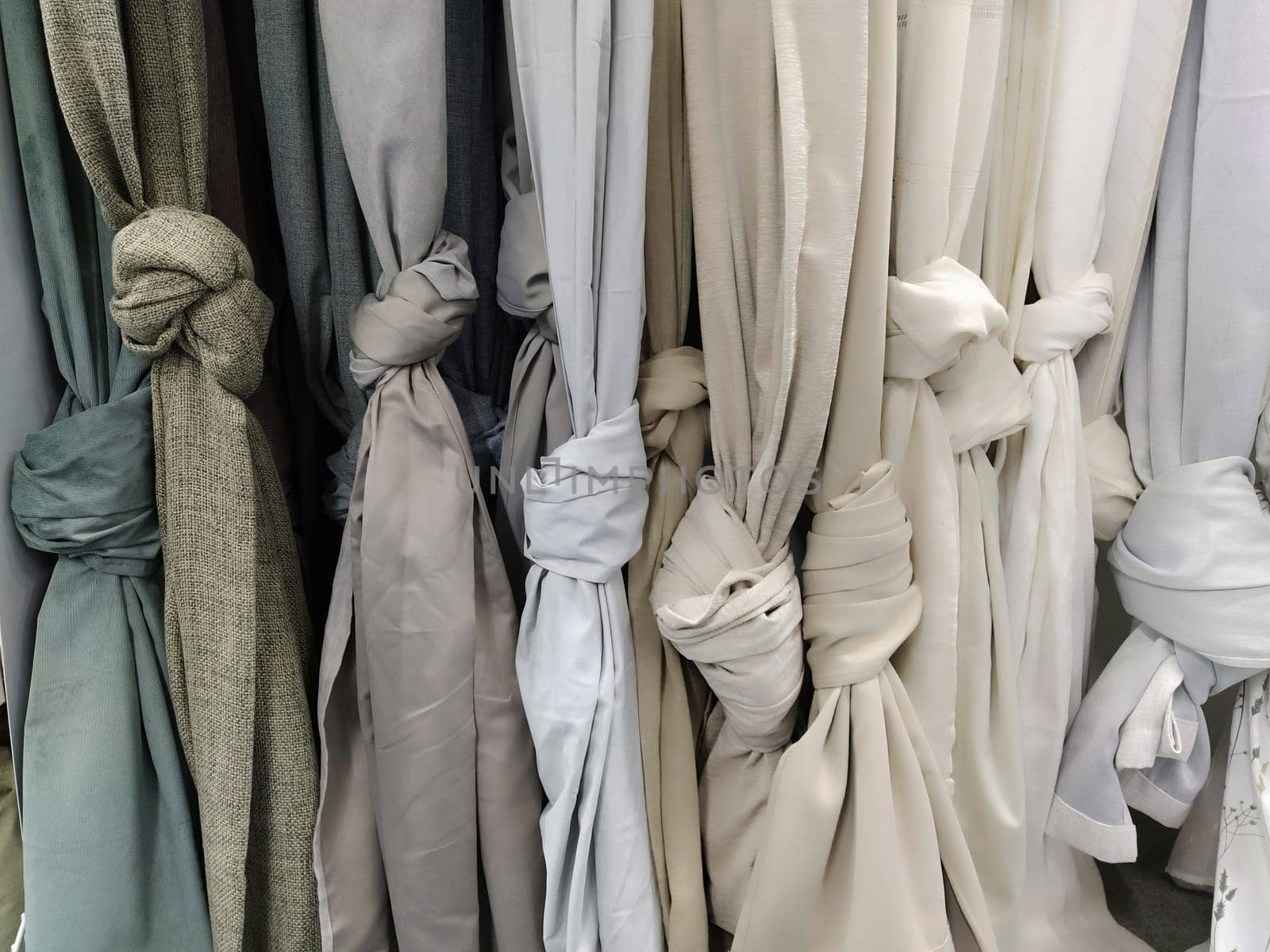 Curtain and fabric for drapery and interior decoration. Samples of gray and white fabrics in the store are hung vertically and tied in knots. Curtains in the showcase