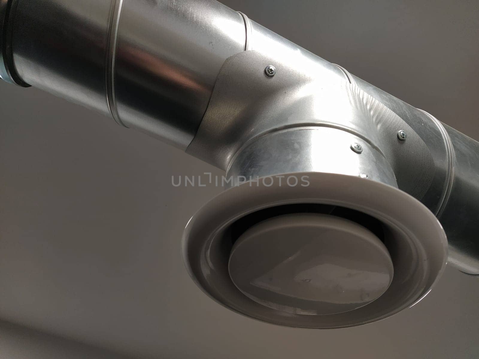 Extractor hood in a public toilet. Round metal pipe with gray air extractor. Engineering ventilation systems. Galvanized pipes under the ceiling of the room. Plastic round tip.