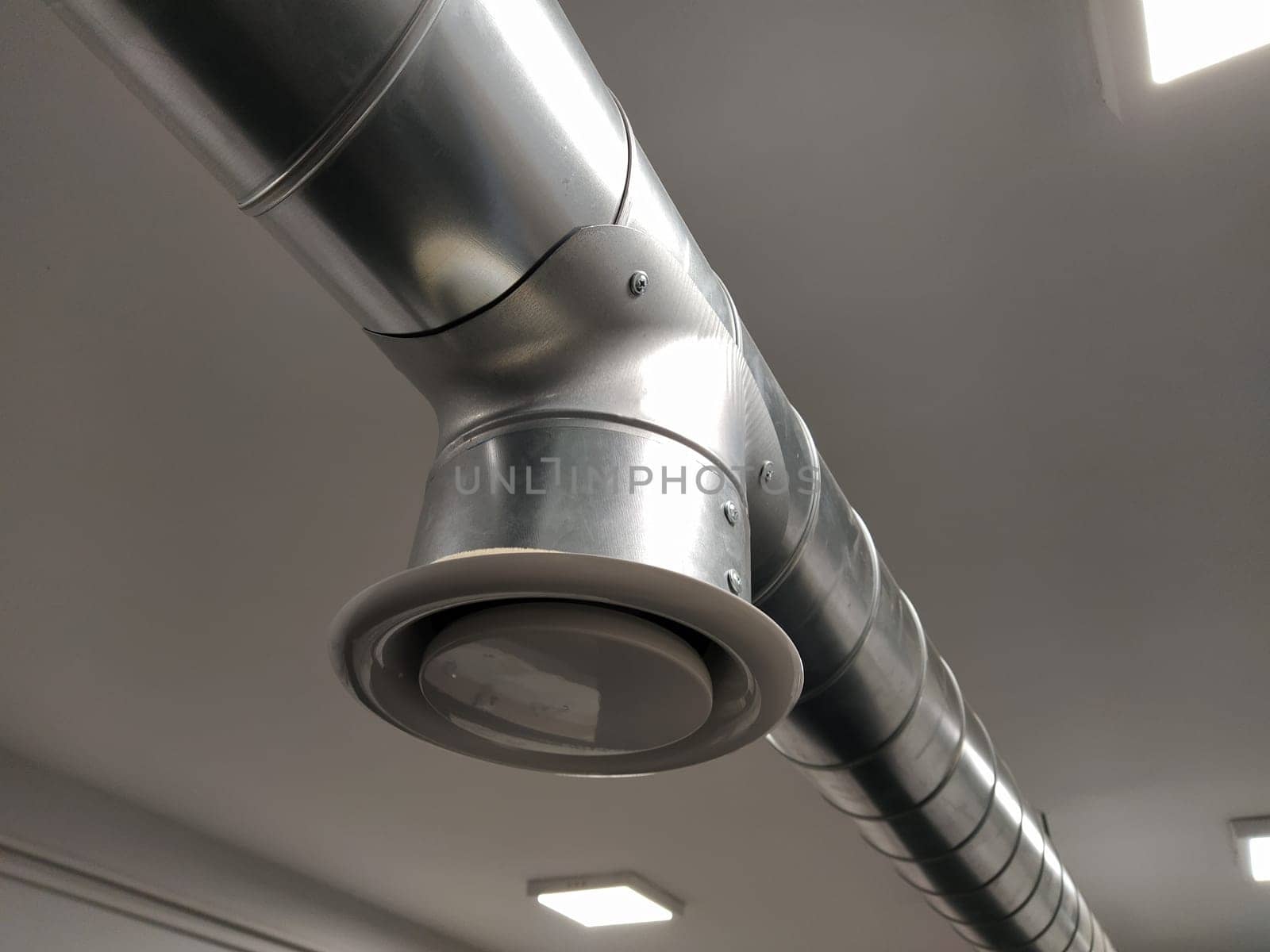 Extractor hood in a public toilet. Round metal pipe with gray air extractor. Engineering ventilation systems. Galvanized pipes under the ceiling of the room. Plastic round tip.