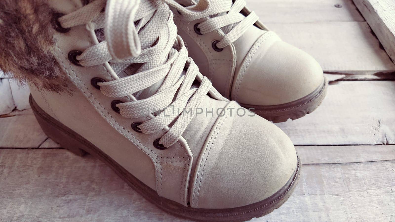 Beige children's boots with laces. Beautiful fashionable leather or suede shoes in a light shade on a wooden background. Exhibition of shoes. Shoes on display or shelf. Sale of shoes