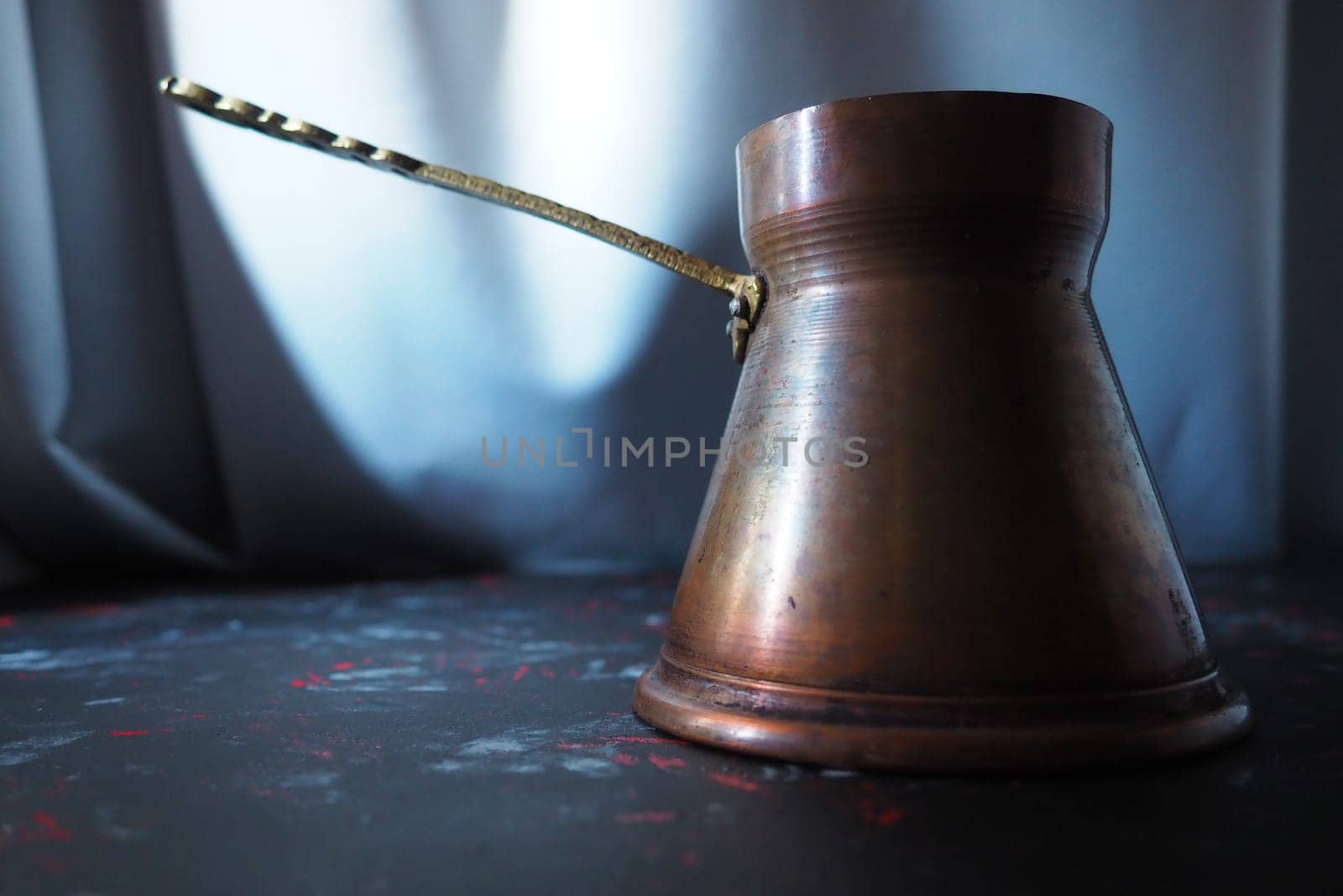 Balkan cezve for turkish coffee. A copper cezve on black surface. Antique bronze utensils. Carved metal handle with pattern. Black background with white, red and blue spots