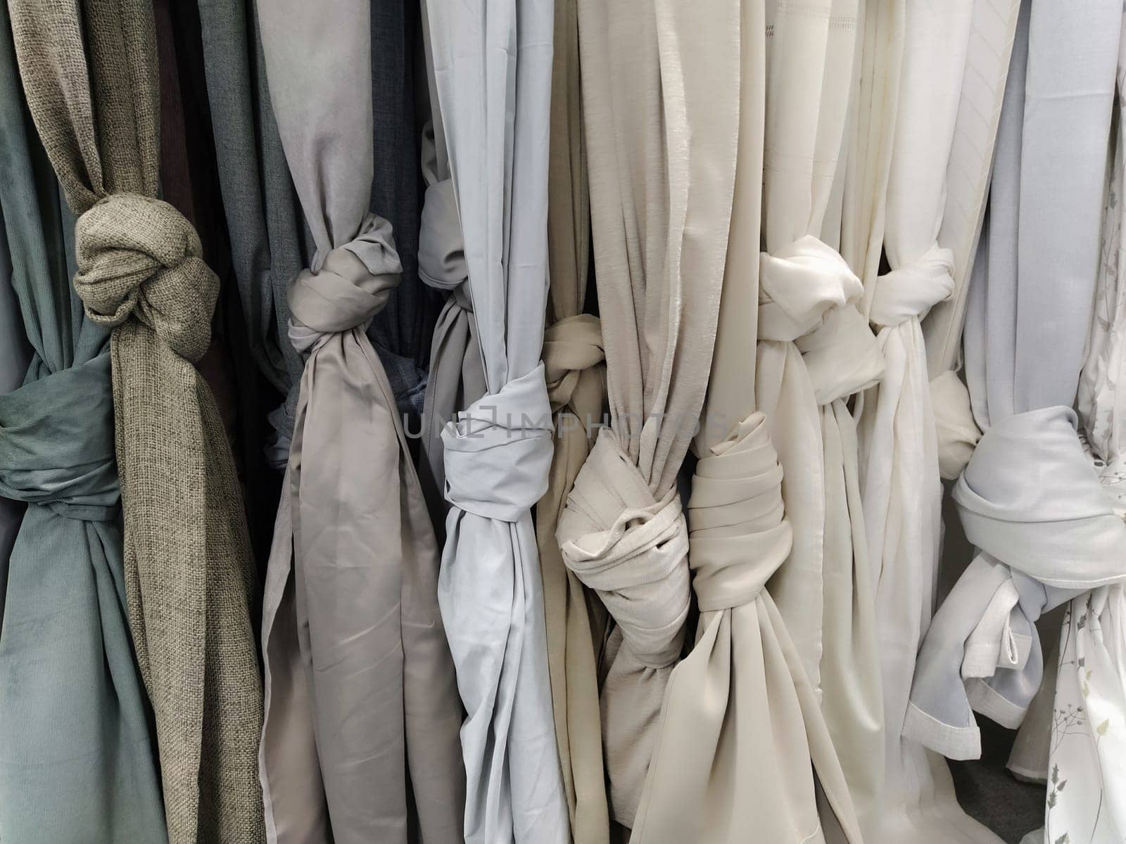 Curtain and fabric for drapery and interior decoration. Samples of gray and white fabrics in the store are hung vertically and tied in knots. Curtains in the showcase.