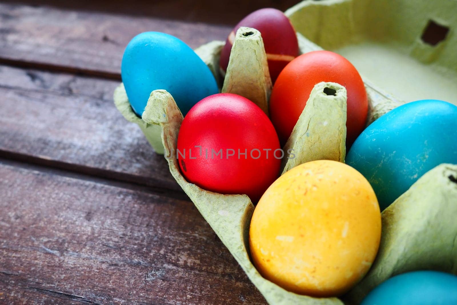 Multi-colored eggs painted with gouache and onion peel in a cardboard box on a wooden table background. Ten boiled eggs. Postcard poster for Easter. Easter holiday. Red, blue, yellow, brown eggs.