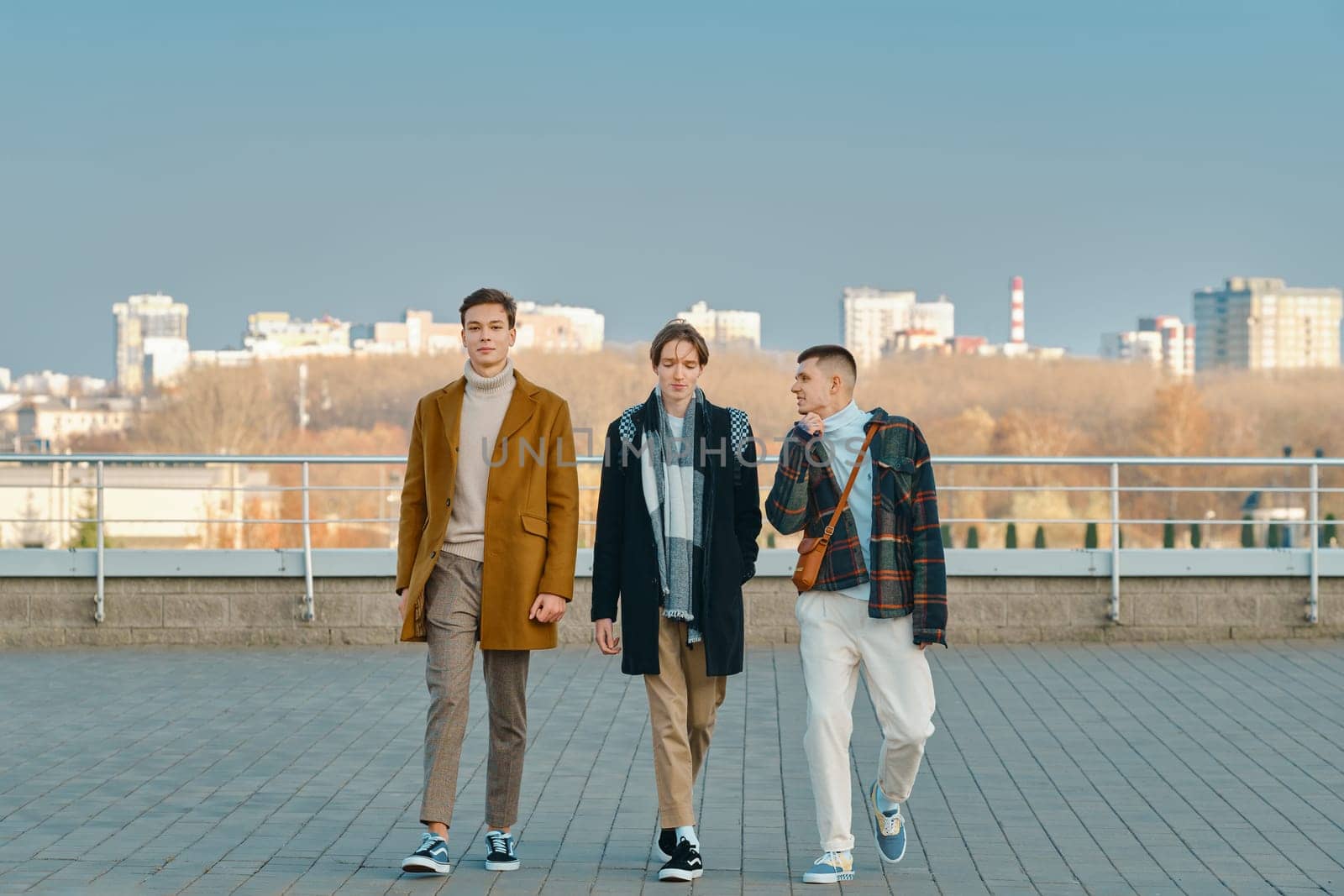 Three young men in autumn clothes are walking down the street