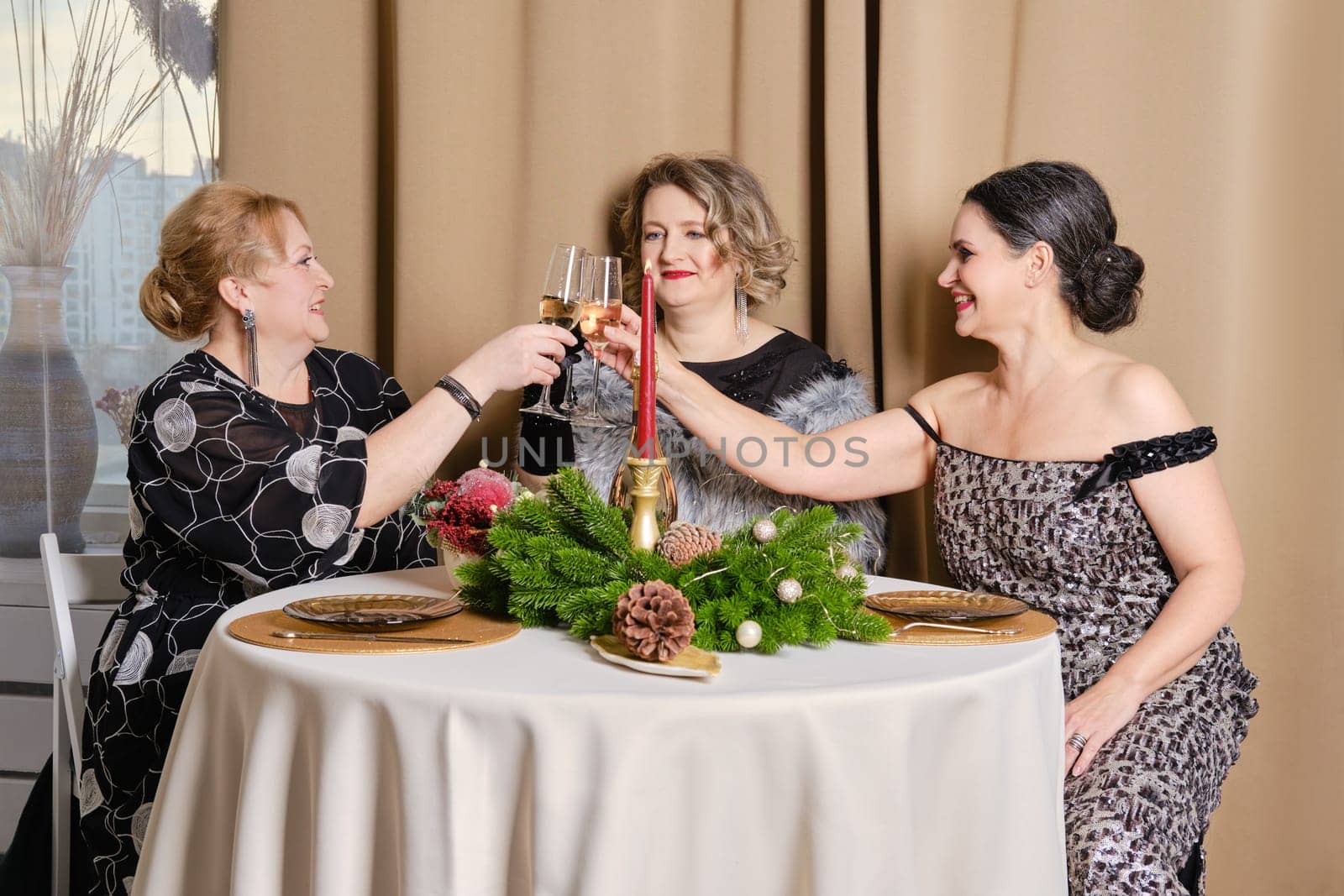 Three juyful middle age women celebrating christmas sitting behind the festive table