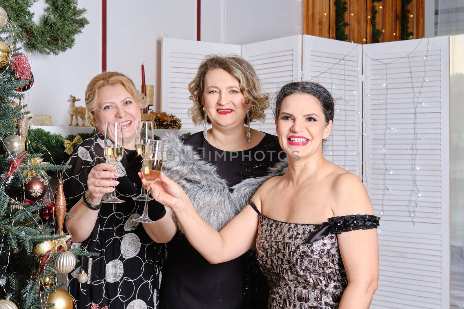 Three joyful middle age women celebrating christmas standing near christmas tree