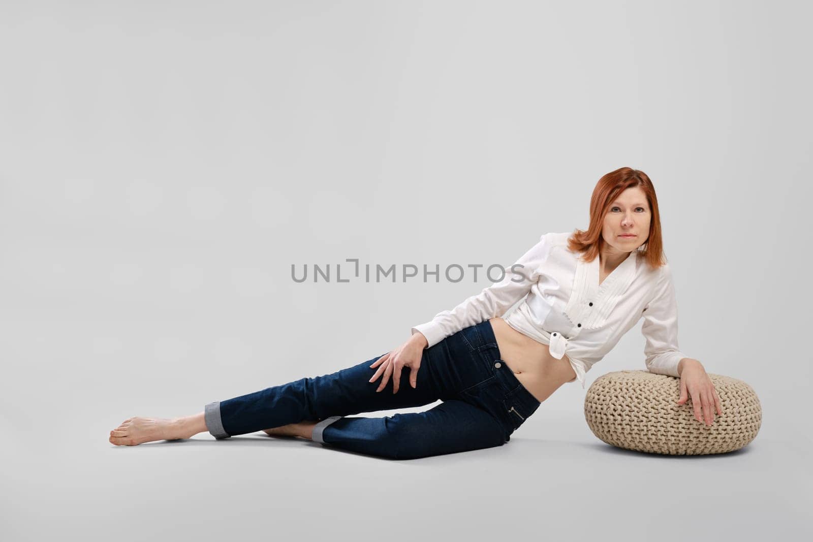 Barefoot middle age woman leaning on padded stool. Studio concept of carefree life.