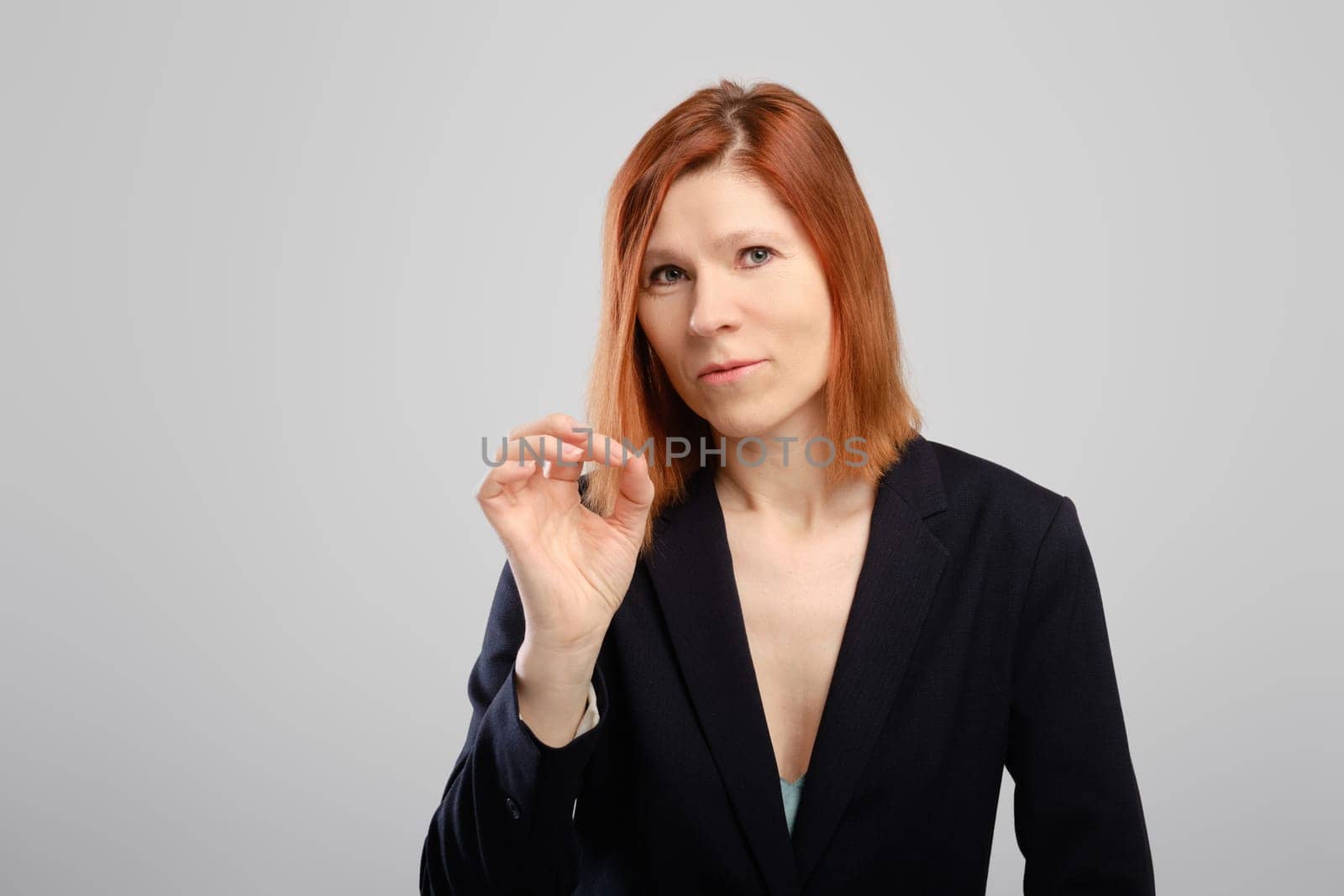 Middle aged woman shows ok gesture over grey studio background, photo with place for text