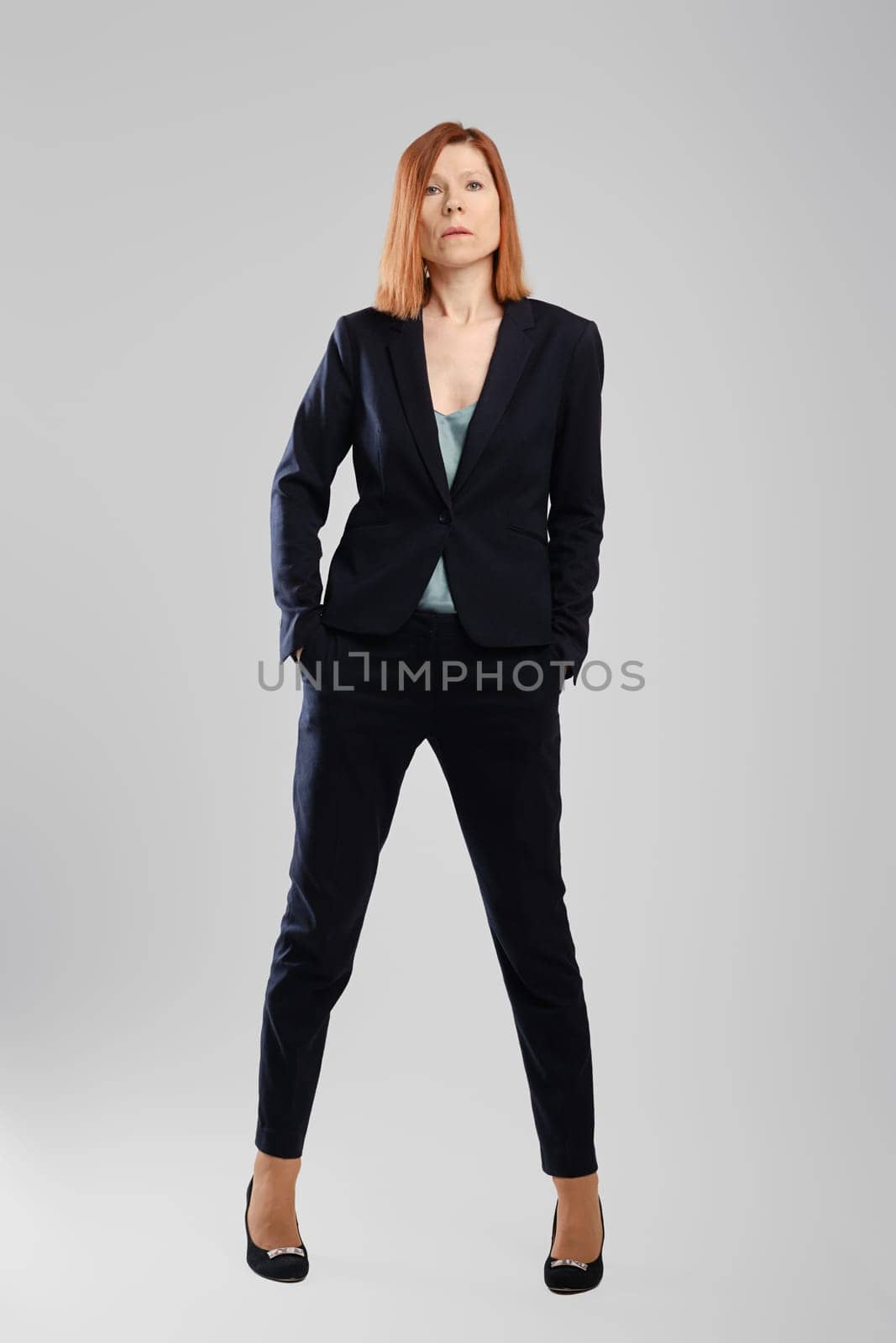 Stylish middle aged woman in pantsuit posing in studio over grey background