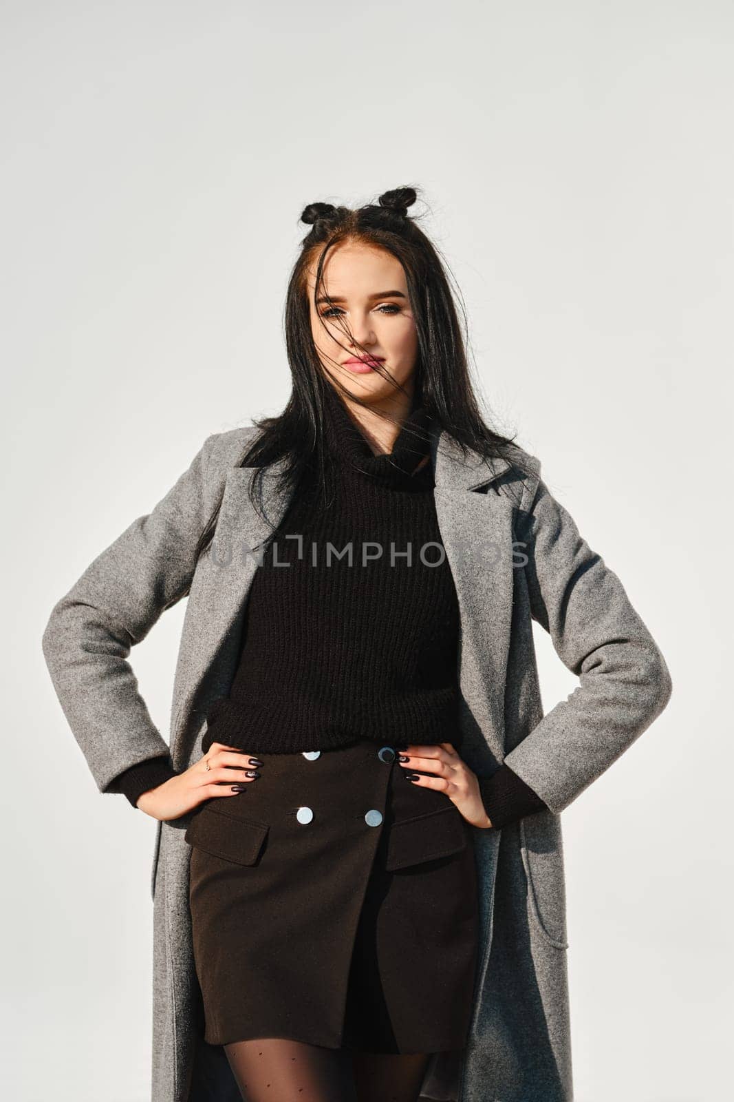 Young woman posing in warm coat with white wall on background in windy day
