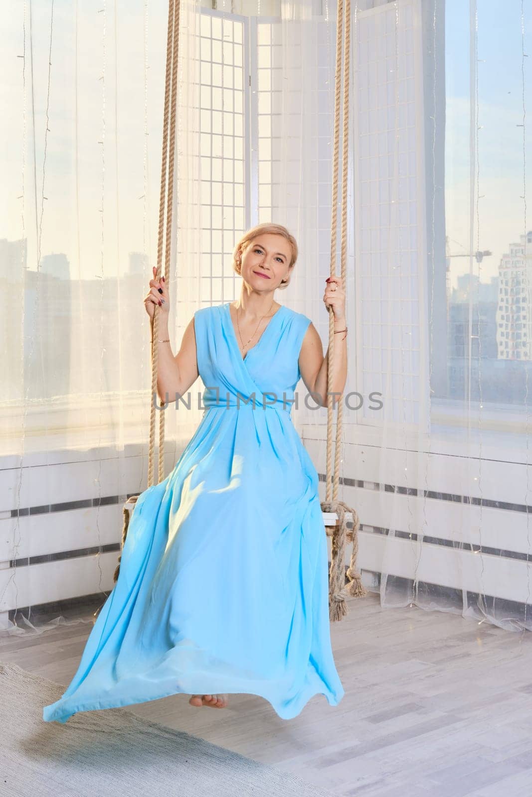 Middle age woman in long blue dress swinging on a home ceiling swing