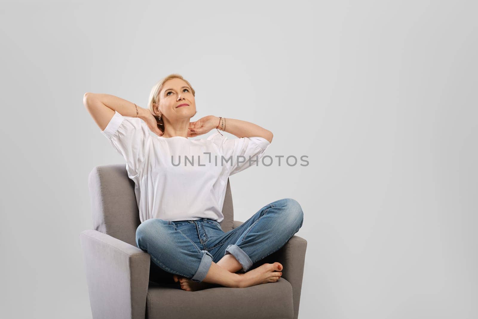Senior woman relaxing in an armchair crossing legs and hold hands behind her head