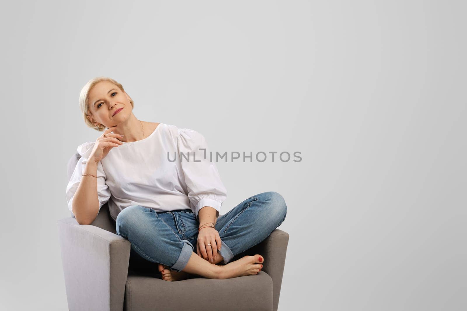 Relaxed senior woman sitting in an armchair crossing legs in studio